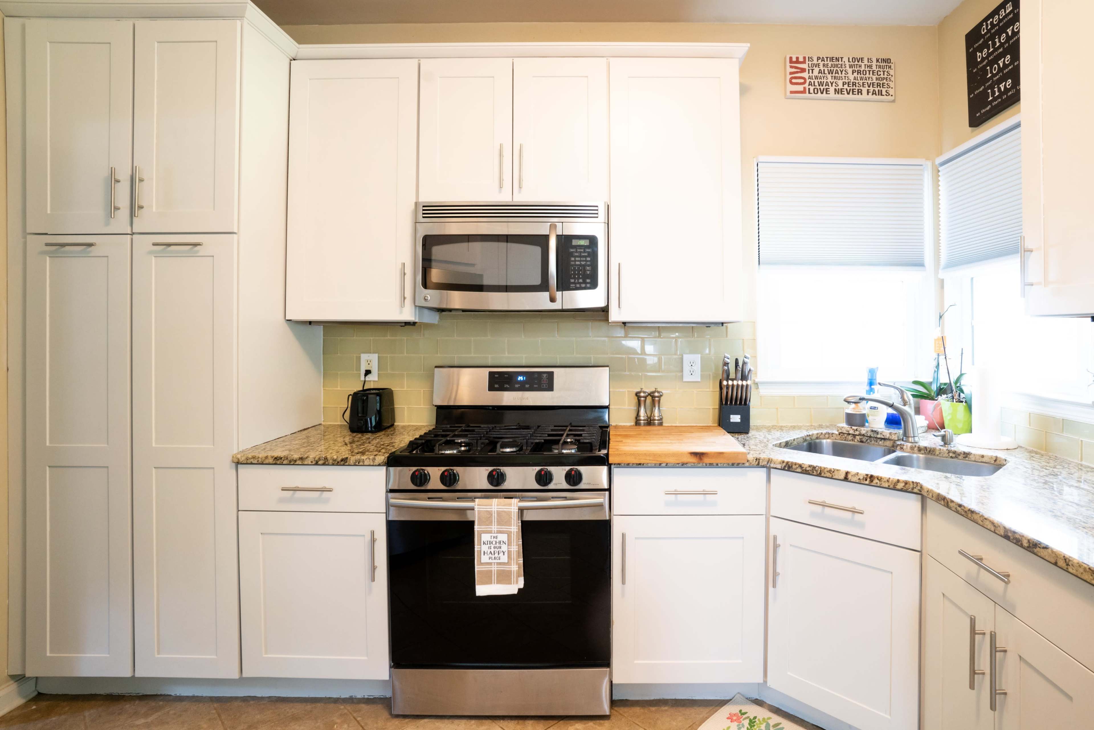 The image depicts a modern kitchen with white cabinetry, a stainless steel oven, and a granite countertop.
