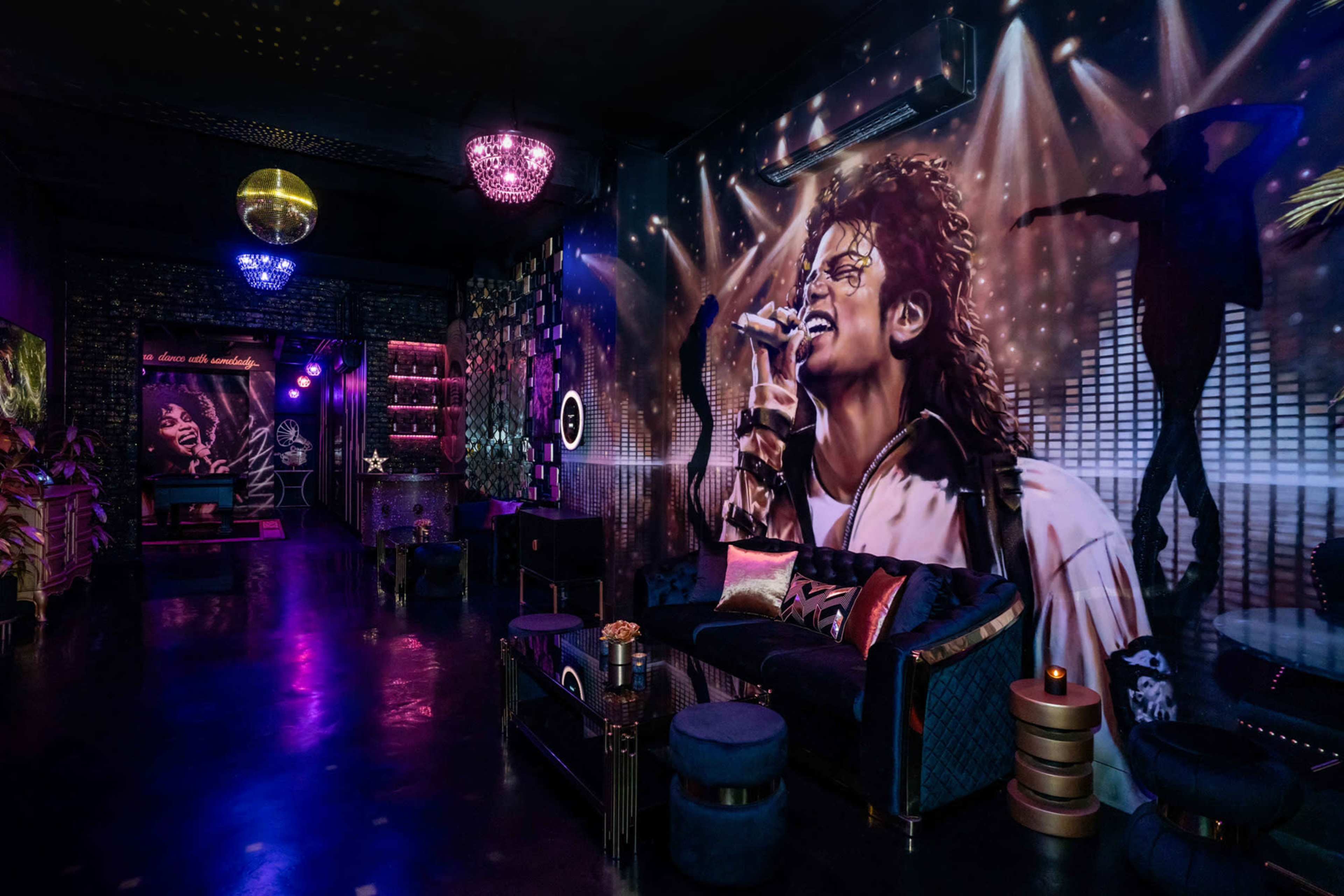 The image shows a dimly lit room decorated with a large mural of a singer, featuring a microphone and vibrant disco lighting.