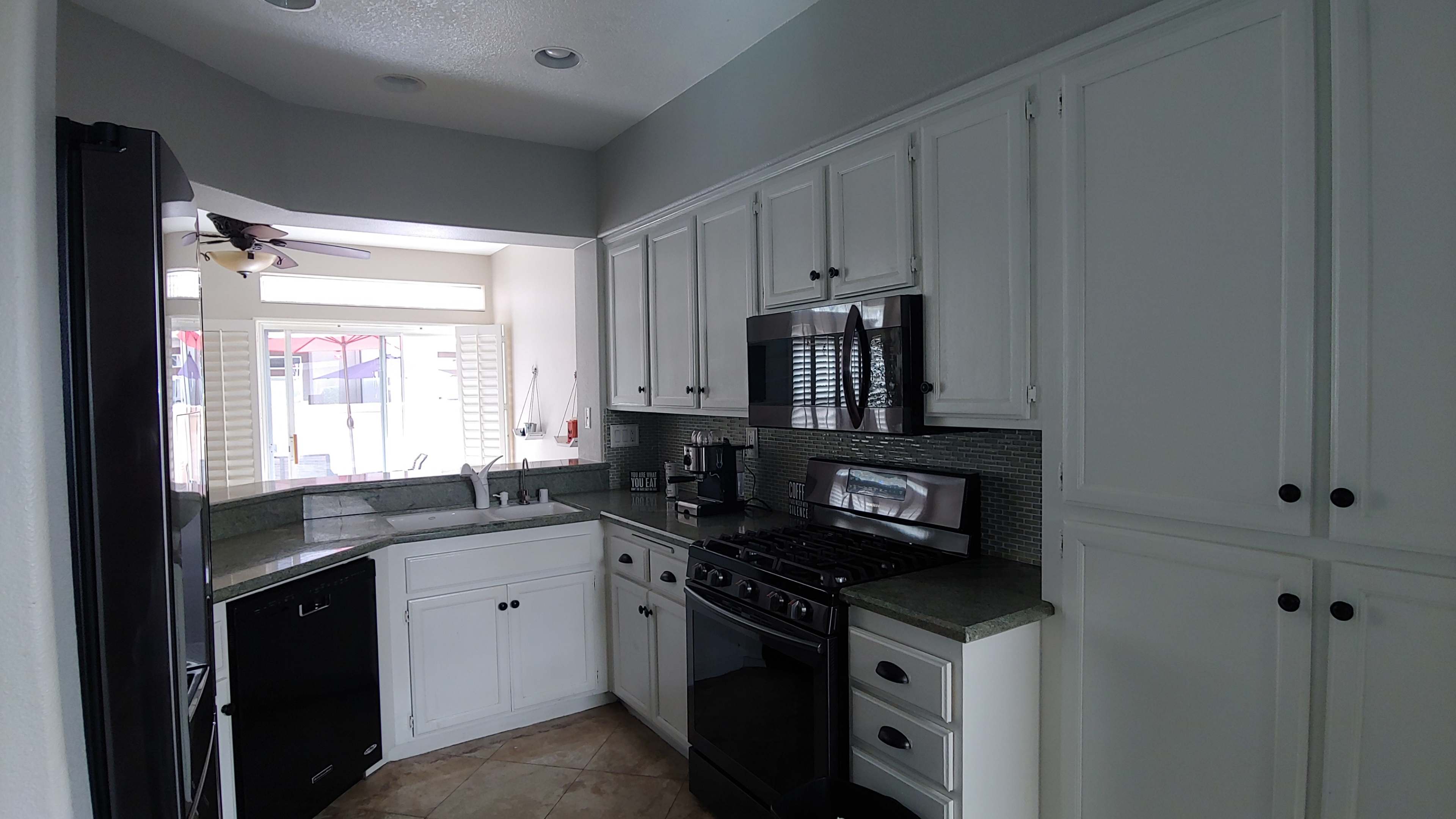 A modern kitchen with white cabinets, a black refrigerator, a stainless steel microwave, and a gas stove.