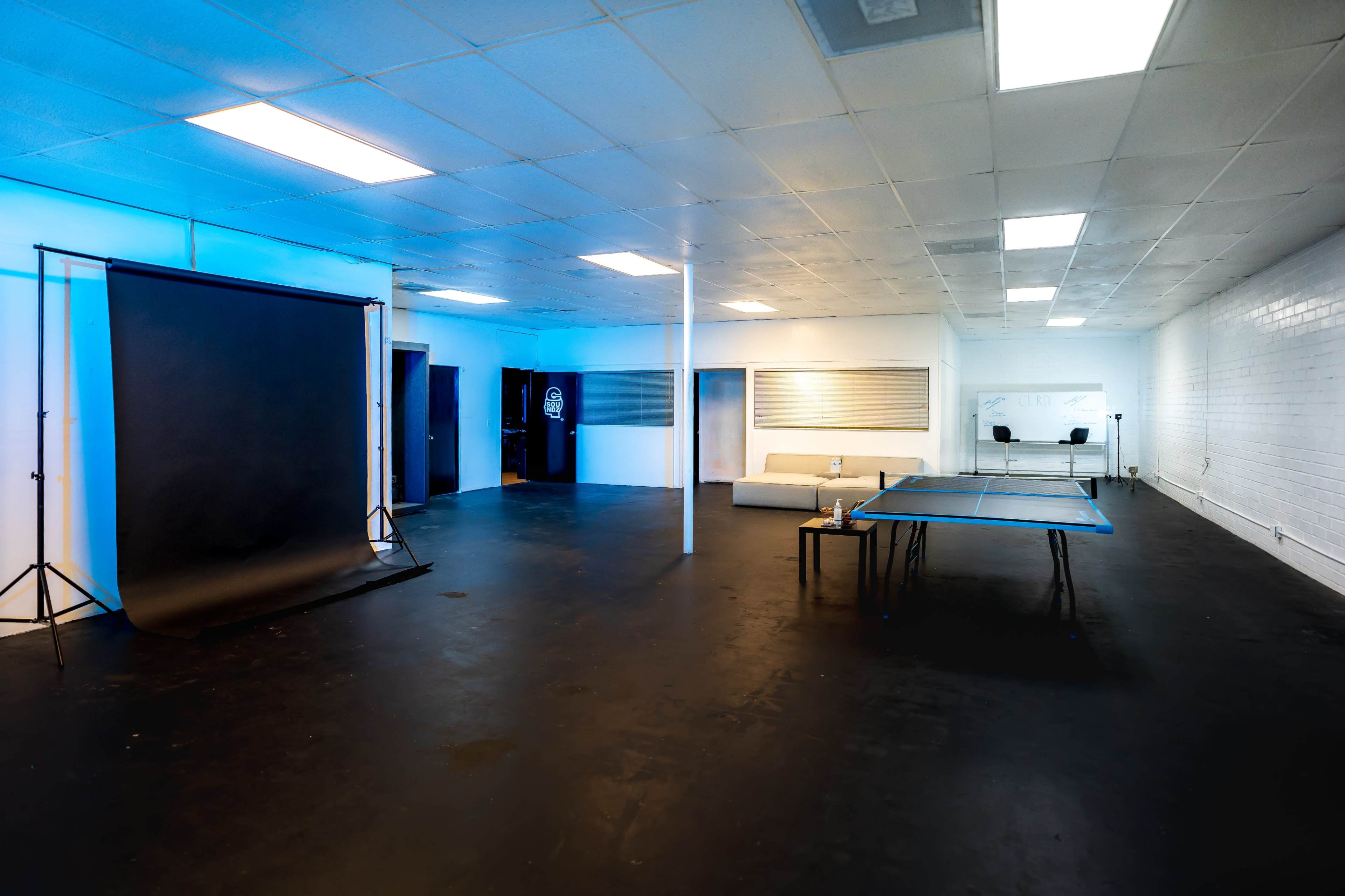 A spacious room with black flooring, featuring a black backdrop on a stand, a ping pong table, and a couch against the wall.