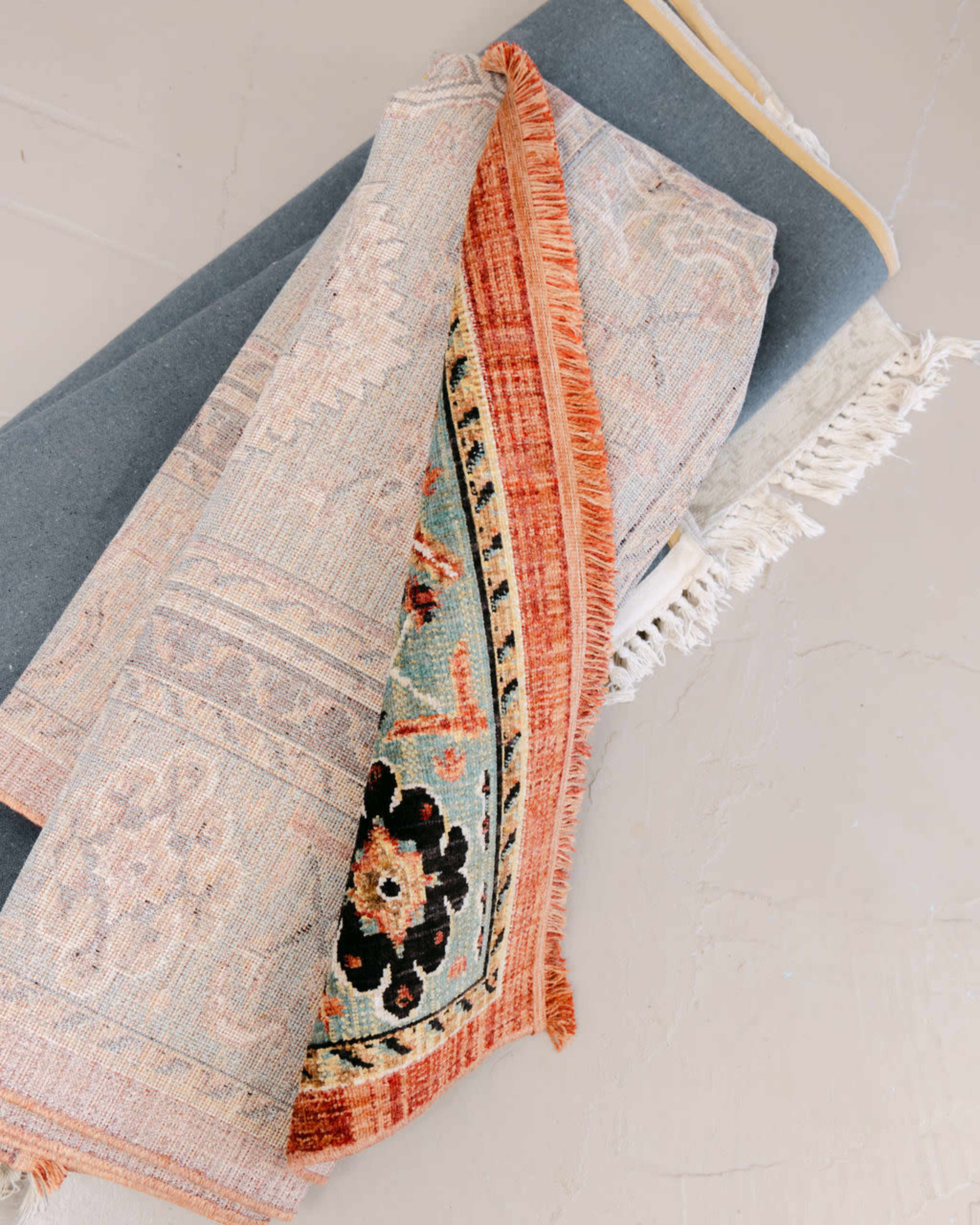 A rolled-up decorative rug is partially unrolled, revealing intricate patterns and colors, alongside another rolled rug on a flat surface.