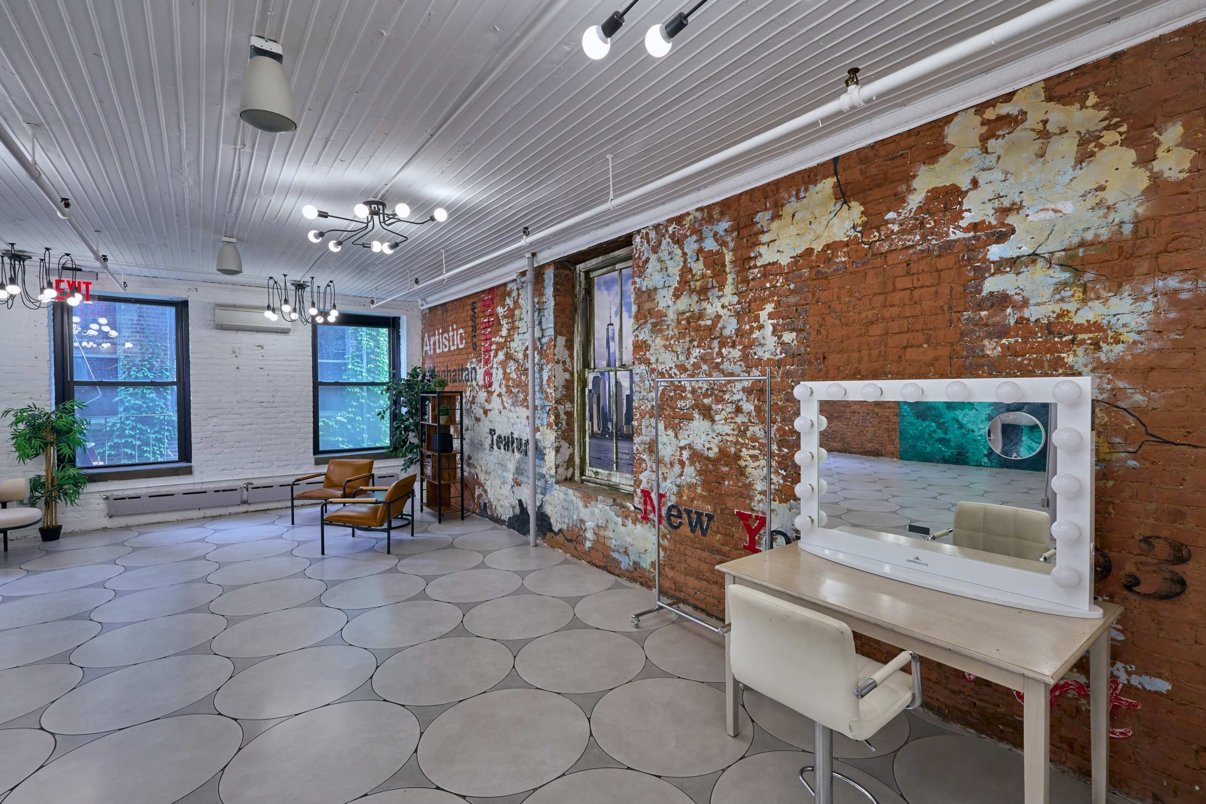A spacious room features a vintage brick wall, a large illuminated vanity mirror, and modern furniture.