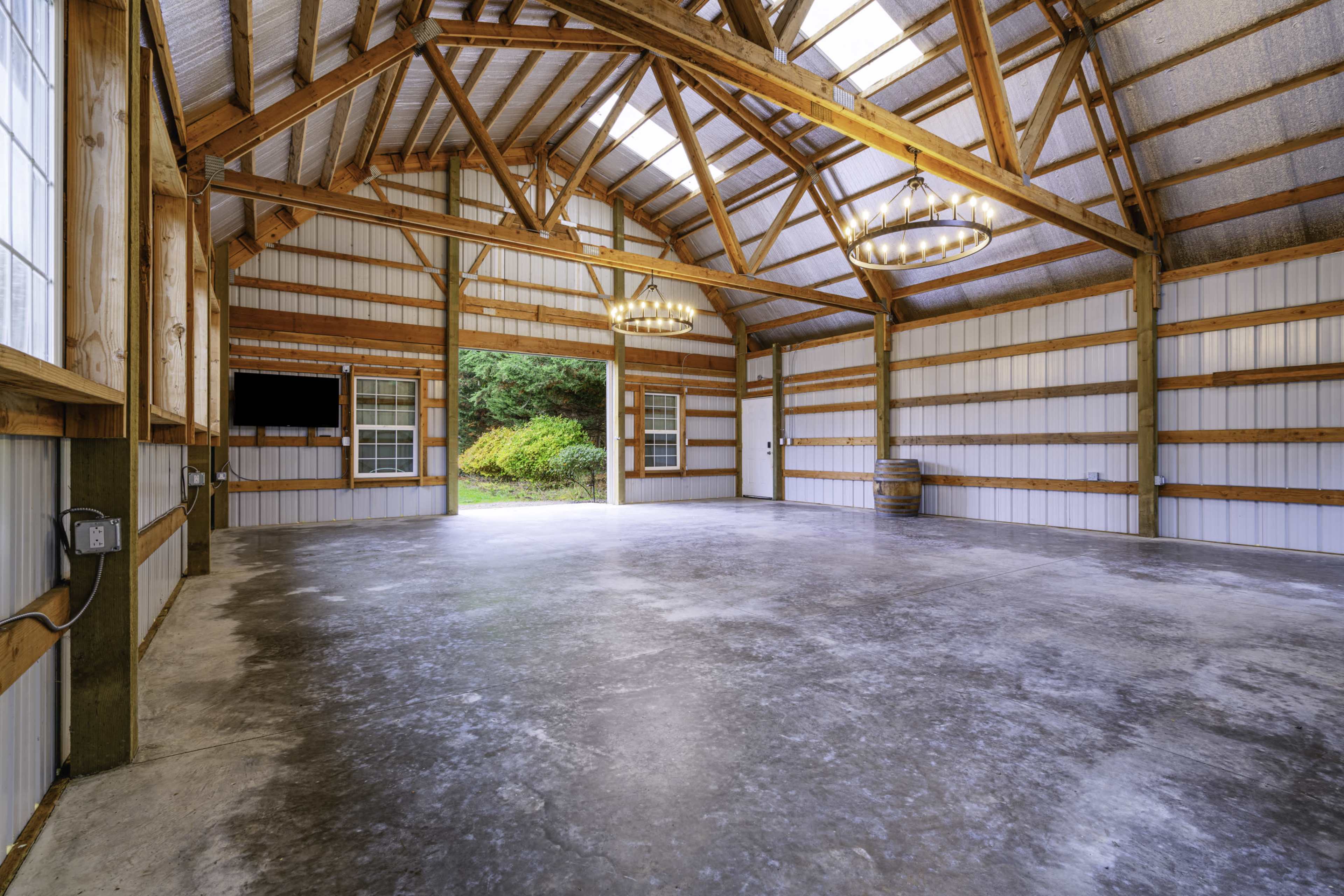 The image shows the interior of a spacious barn with wooden beams, high ceilings, and a polished concrete floor, illuminated by natural light from large windows.