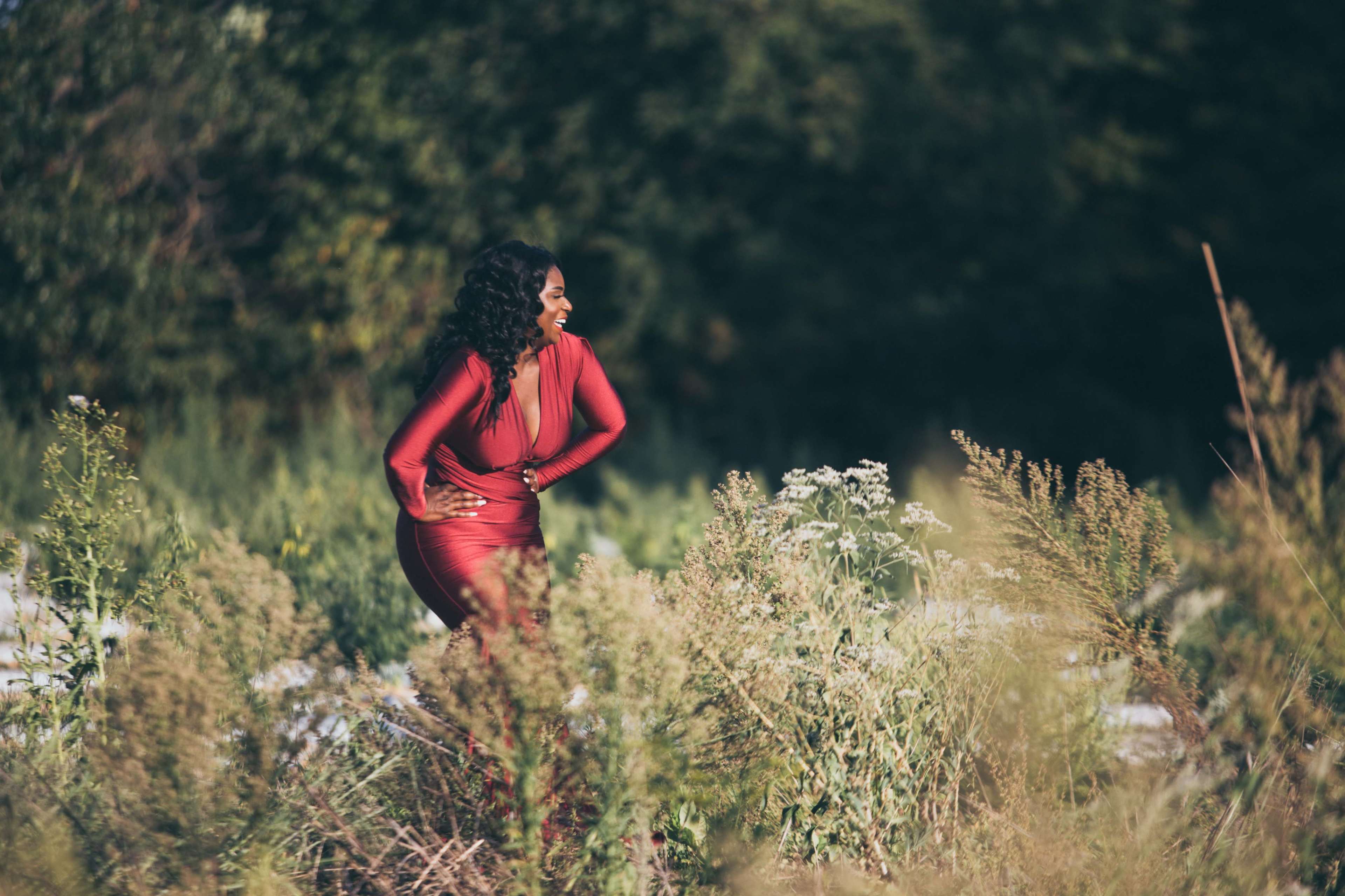 A woman in a red dress stands in a field surrounded by tall grass and wildflowers.