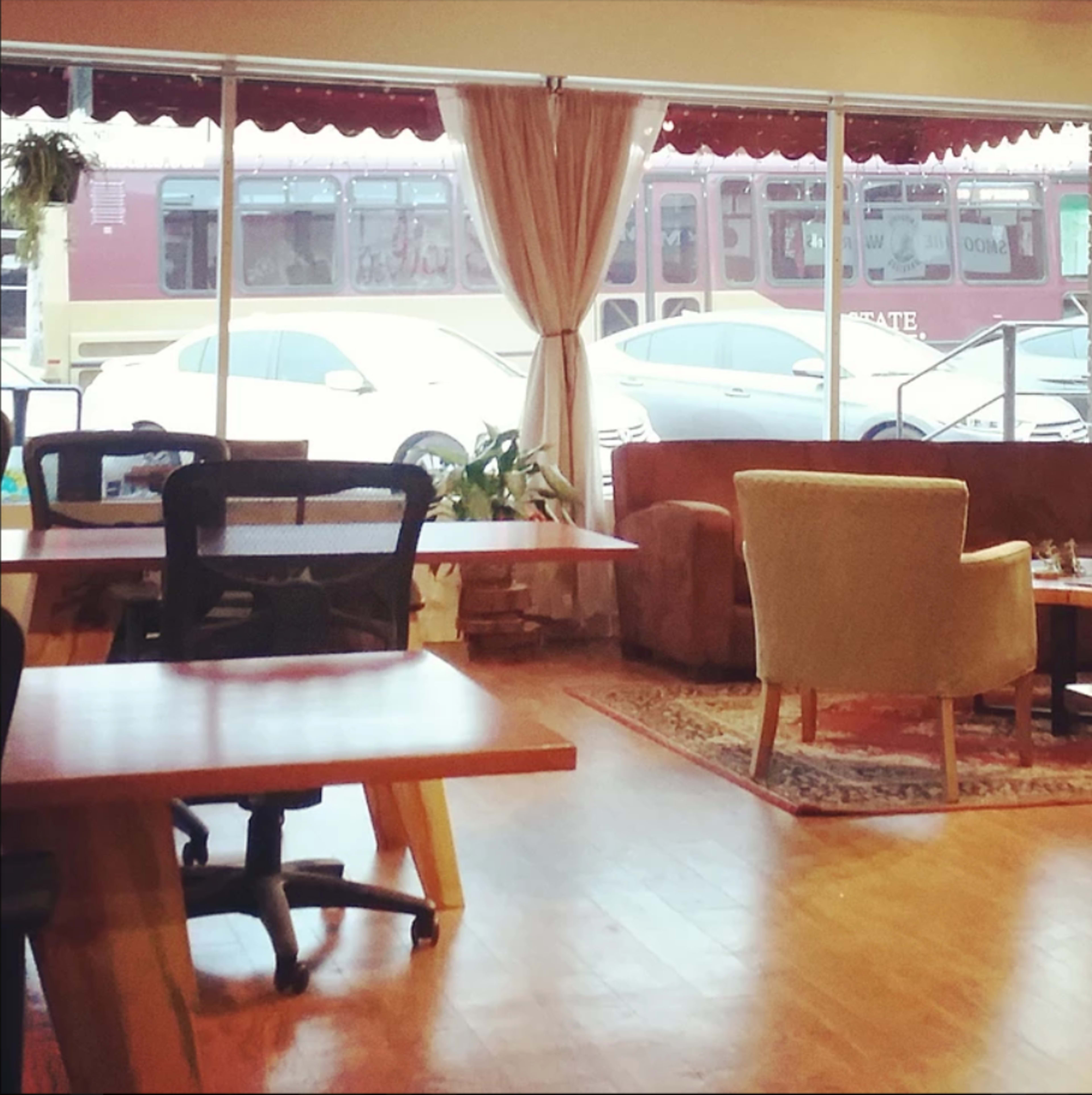 A cozy café interior with several tables, chairs, and large windows facing a street.