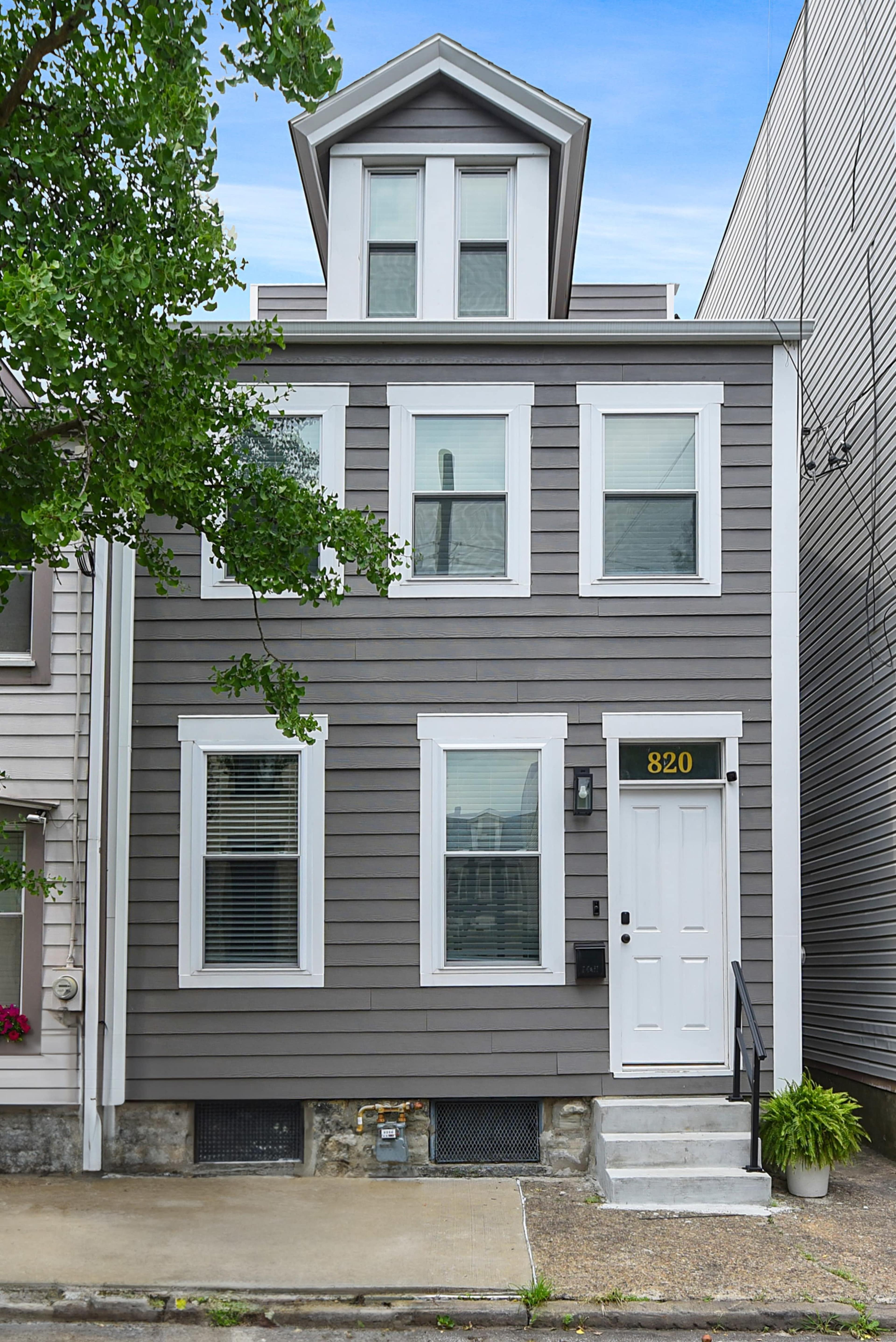 The image shows a two-story gray house with white trim and a front door on the left side, featuring a small flight of steps and a number "820" displayed prominently.