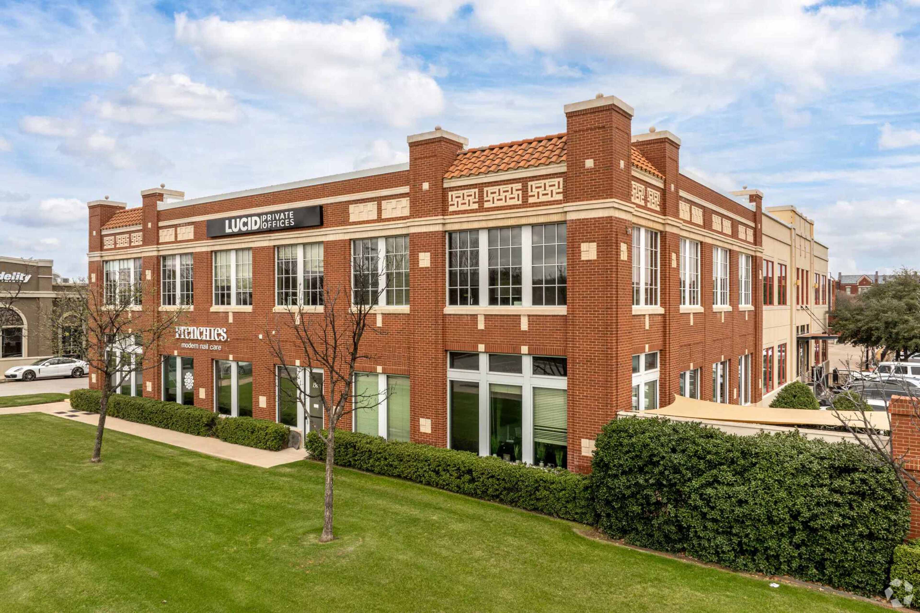 The image shows a three-story brick office building with large windows and landscaping in front, displaying a sign for "LUCID" on the upper level.