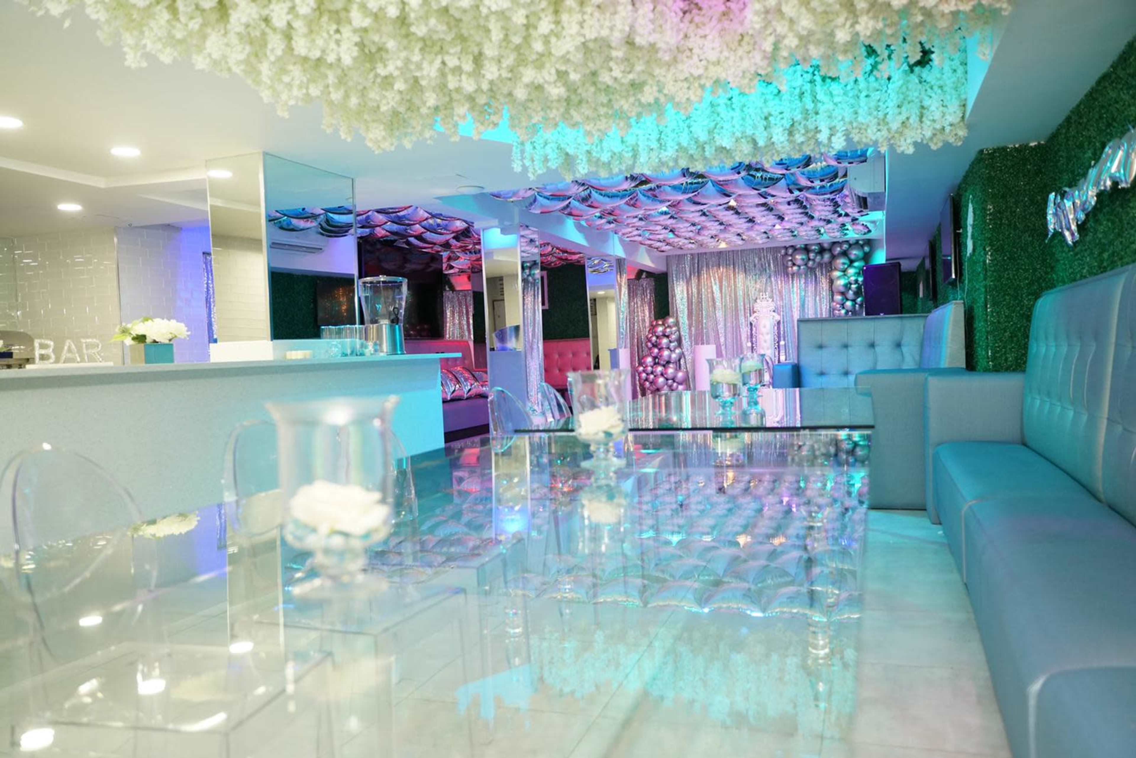 A modern lounge area features transparent furniture, floral decorations overhead, and colorful lighting accents.