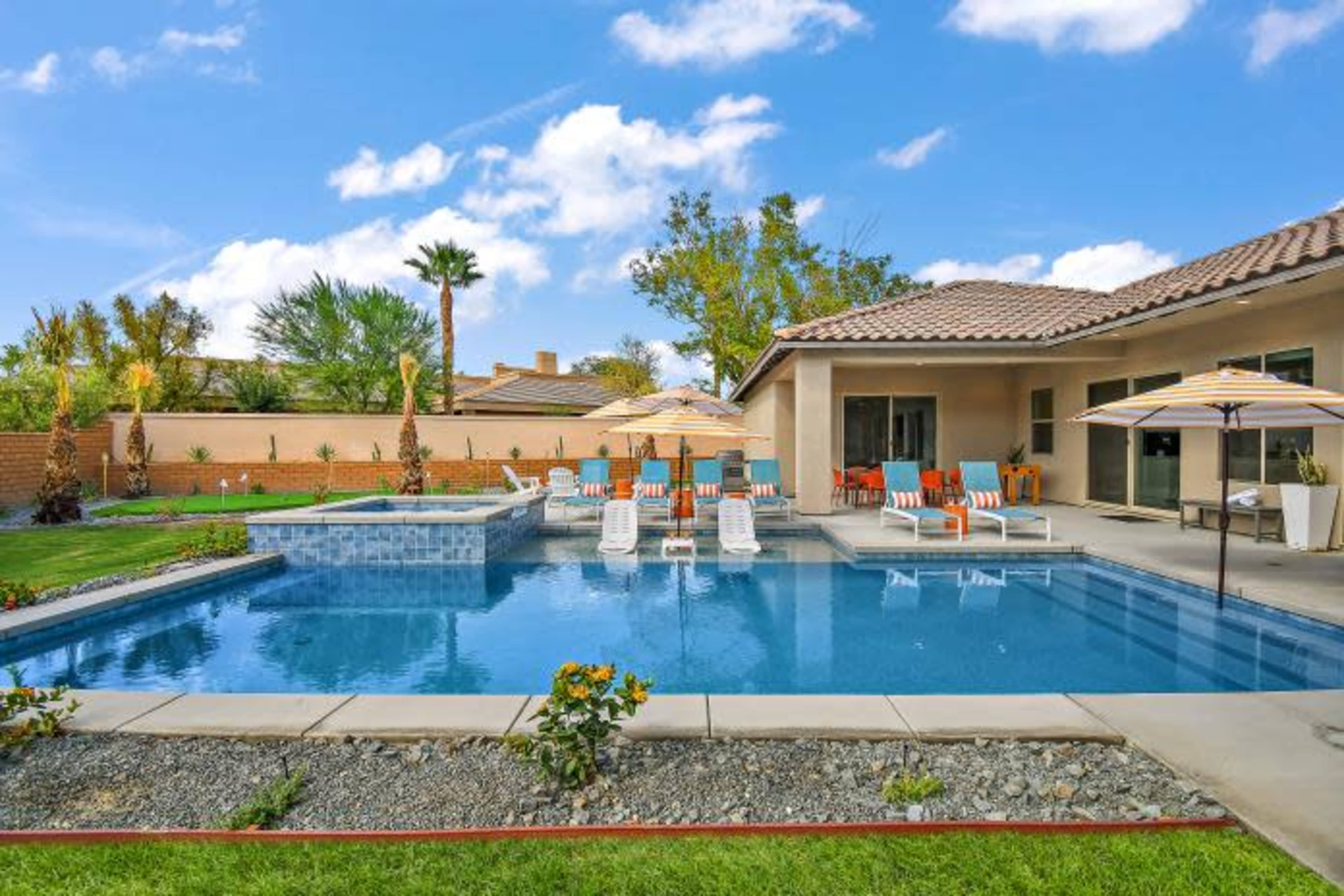 A backyard with a swimming pool, lounge chairs, umbrellas, and a landscaped garden.