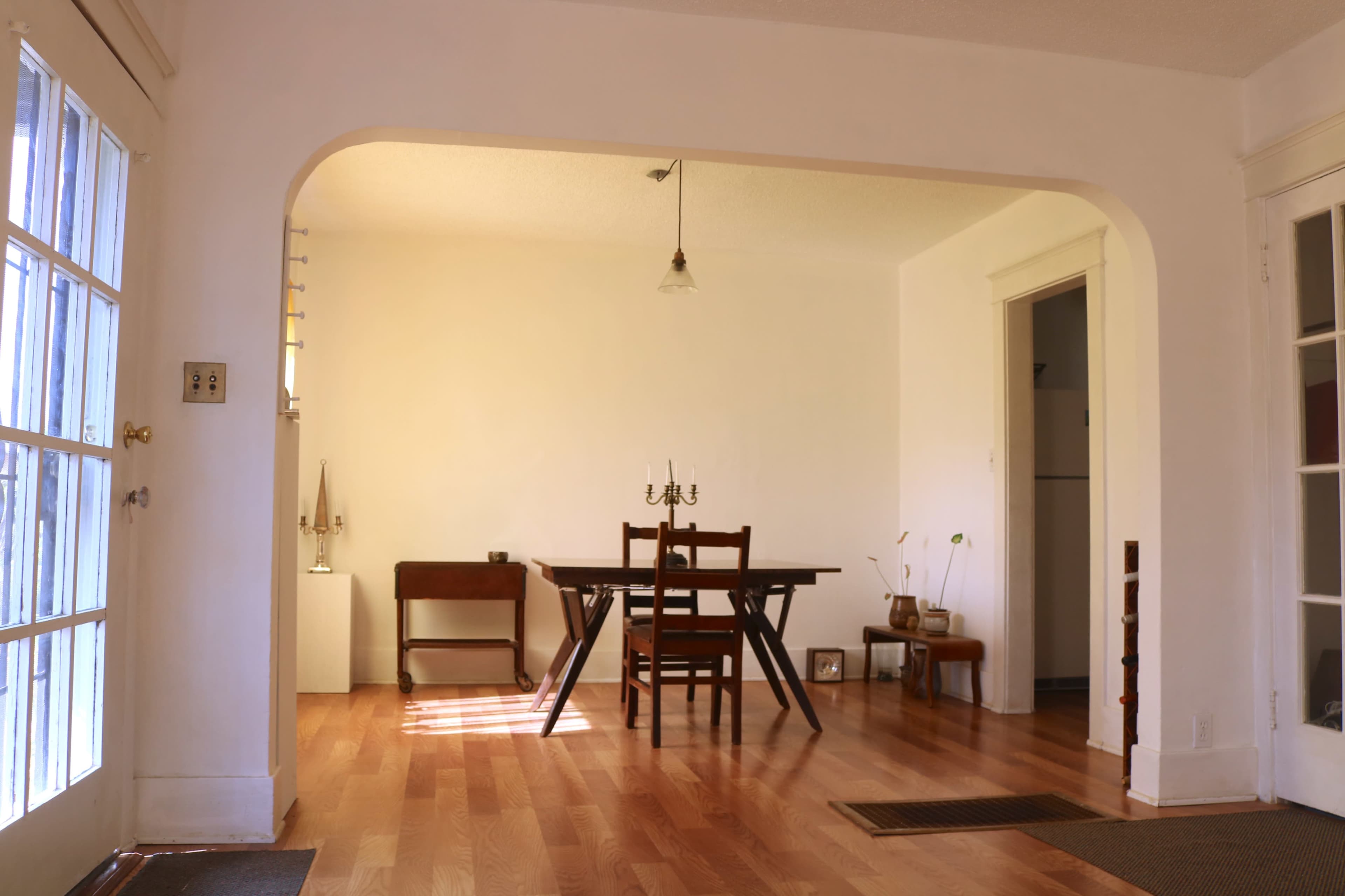 A minimalist dining area with a wooden table and chairs, located in a bright, open space featuring hardwood floors and large windows.