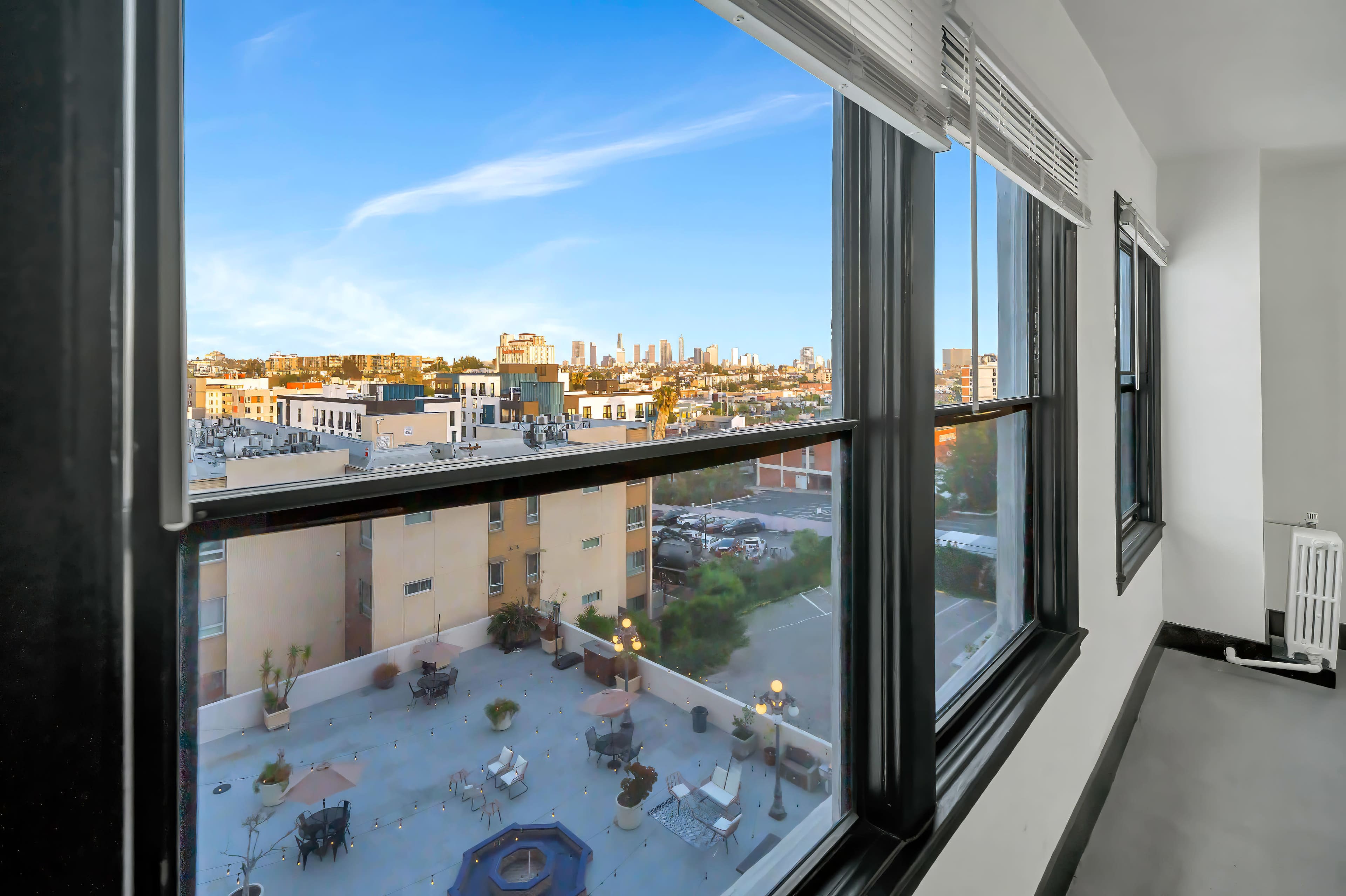 The image shows a view from a window overlooking a cityscape with buildings and a clear blue sky.