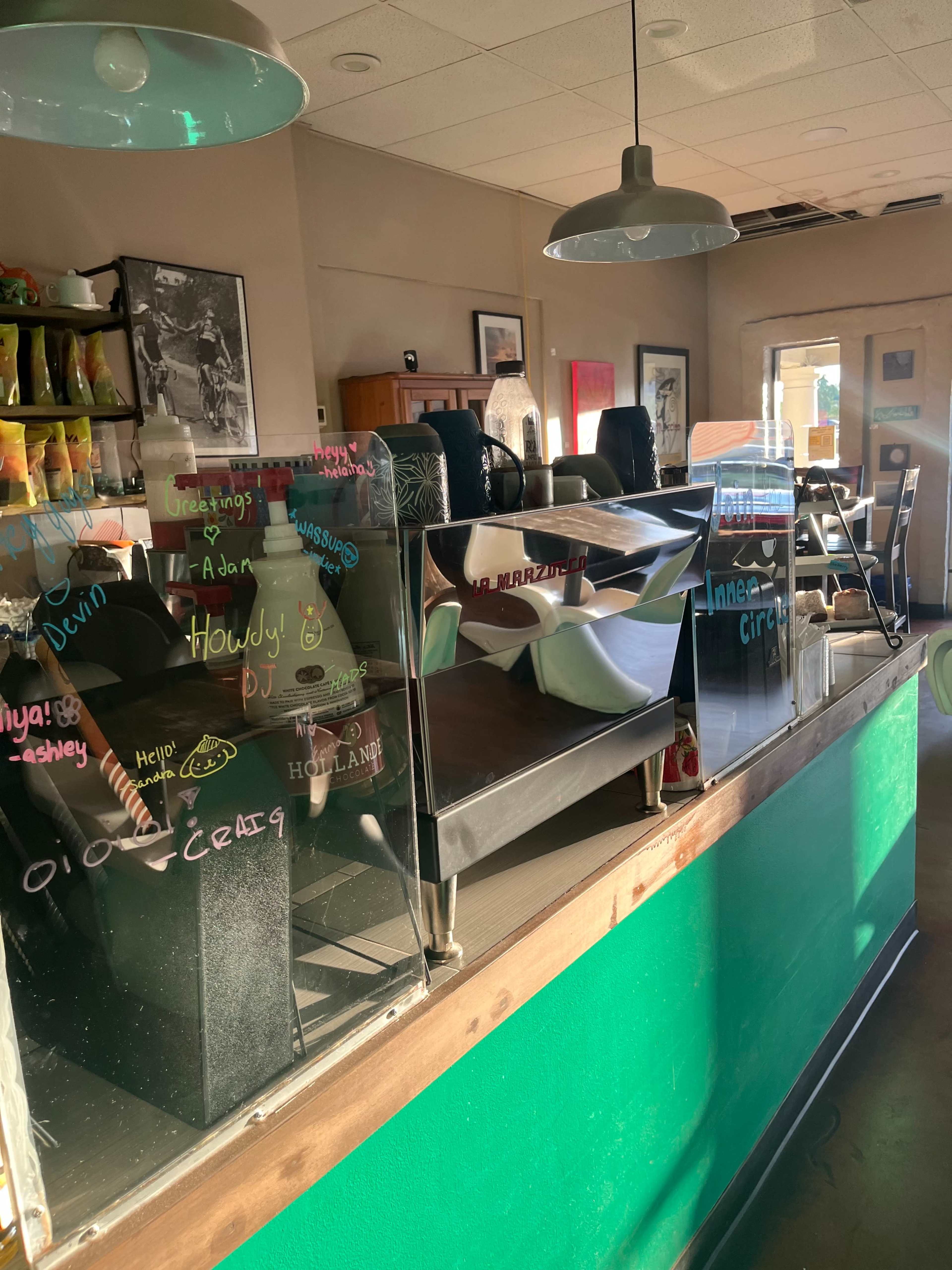 A restaurant interior with tables and chairs, and a counter displaying handwritten messages on the glass partition.