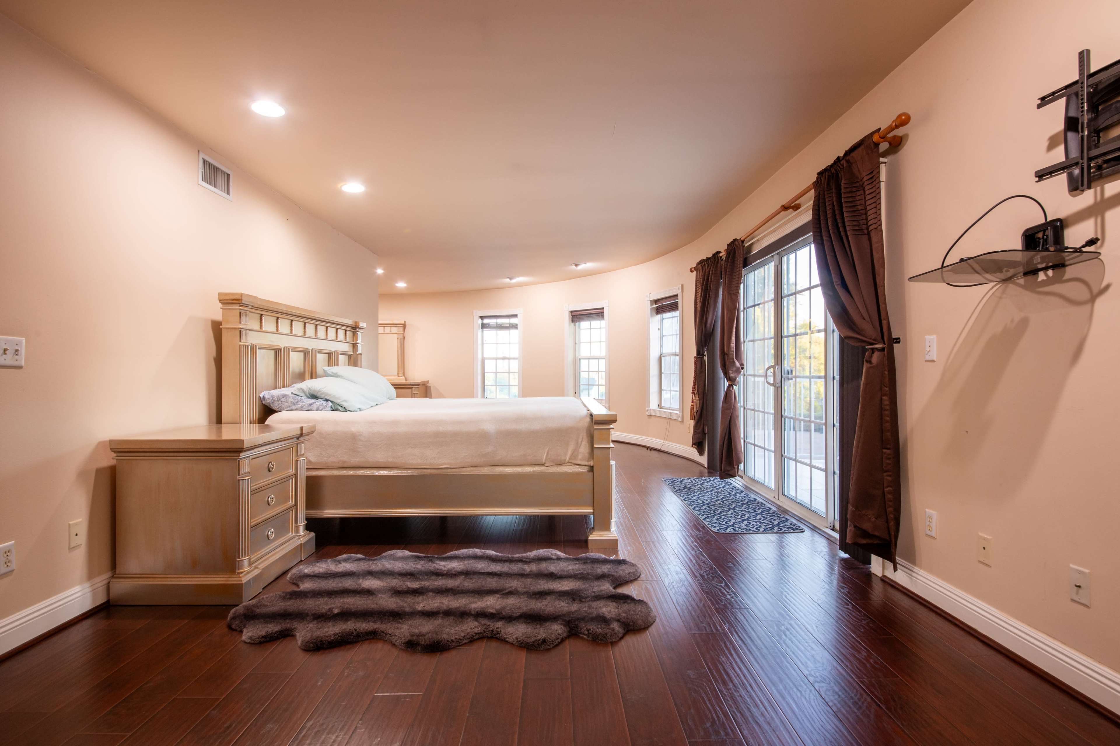 A spacious bedroom featuring a bed with a wooden frame, a nightstand, and large windows that provide access to an outdoor area.