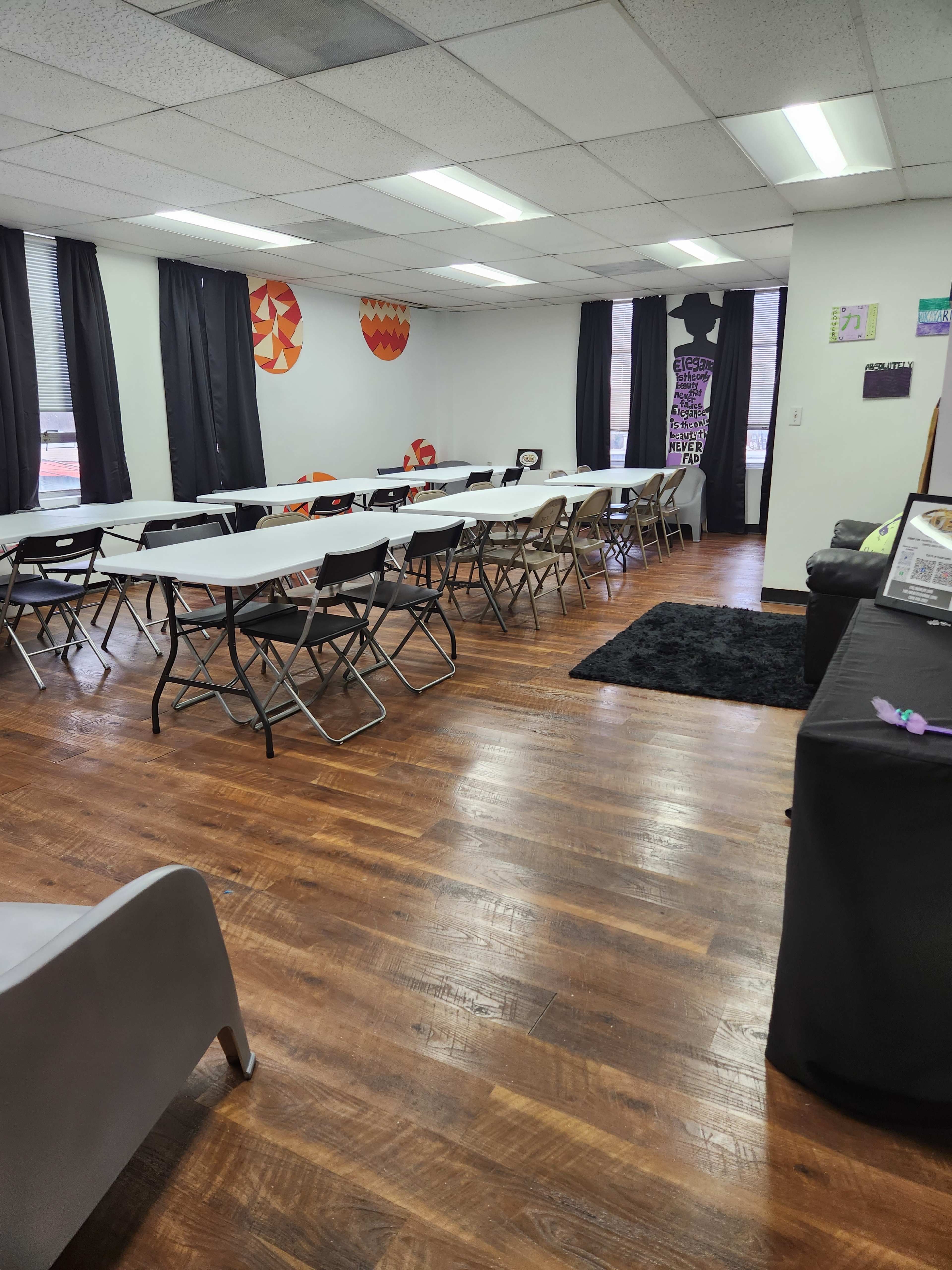 A classroom with rows of tables and chairs, black curtains on the windows, and artwork on the walls.