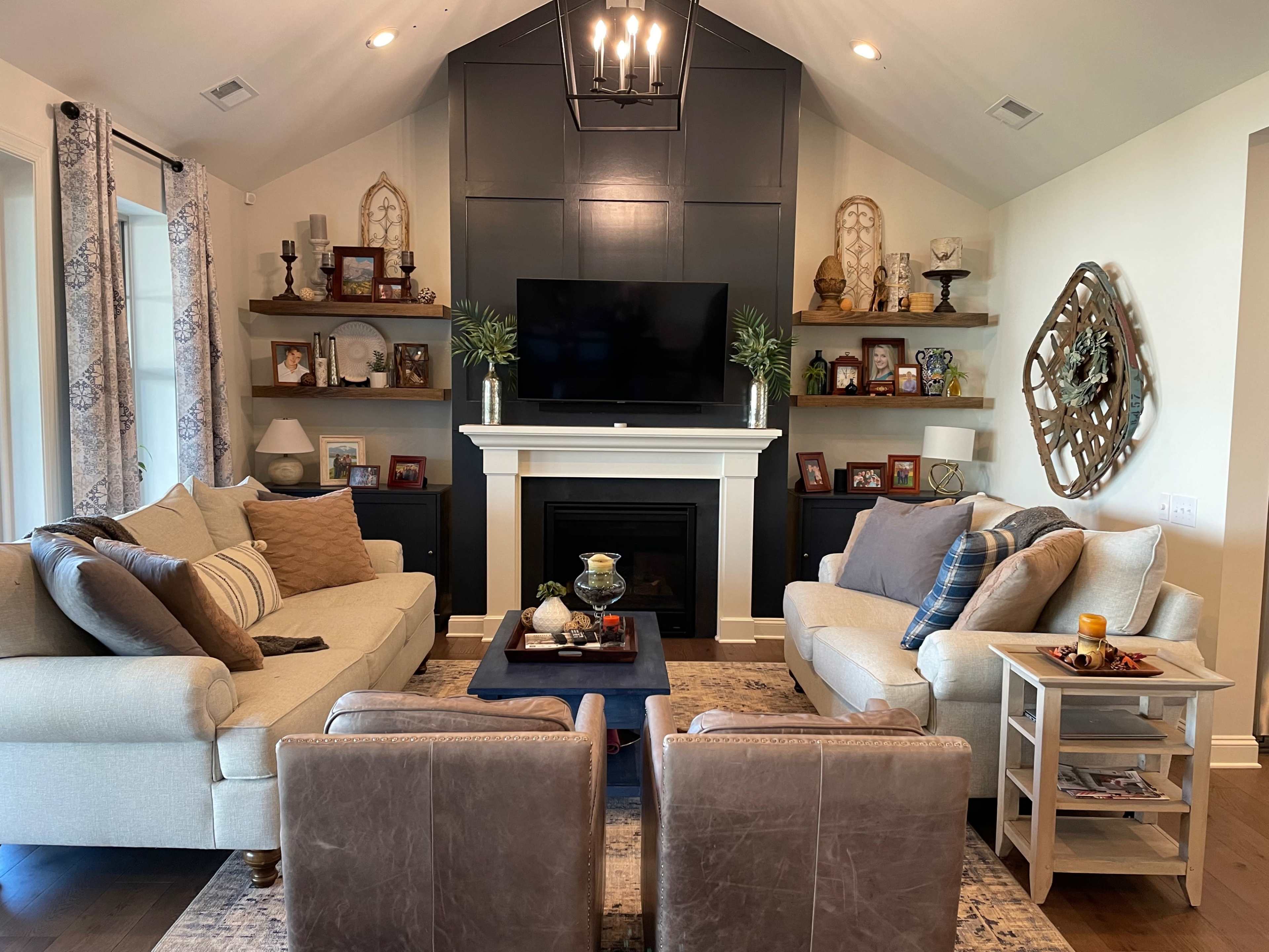 A cozy living room with two sofas, two armchairs, and a fireplace surrounded by shelves displaying photographs and decorative items.