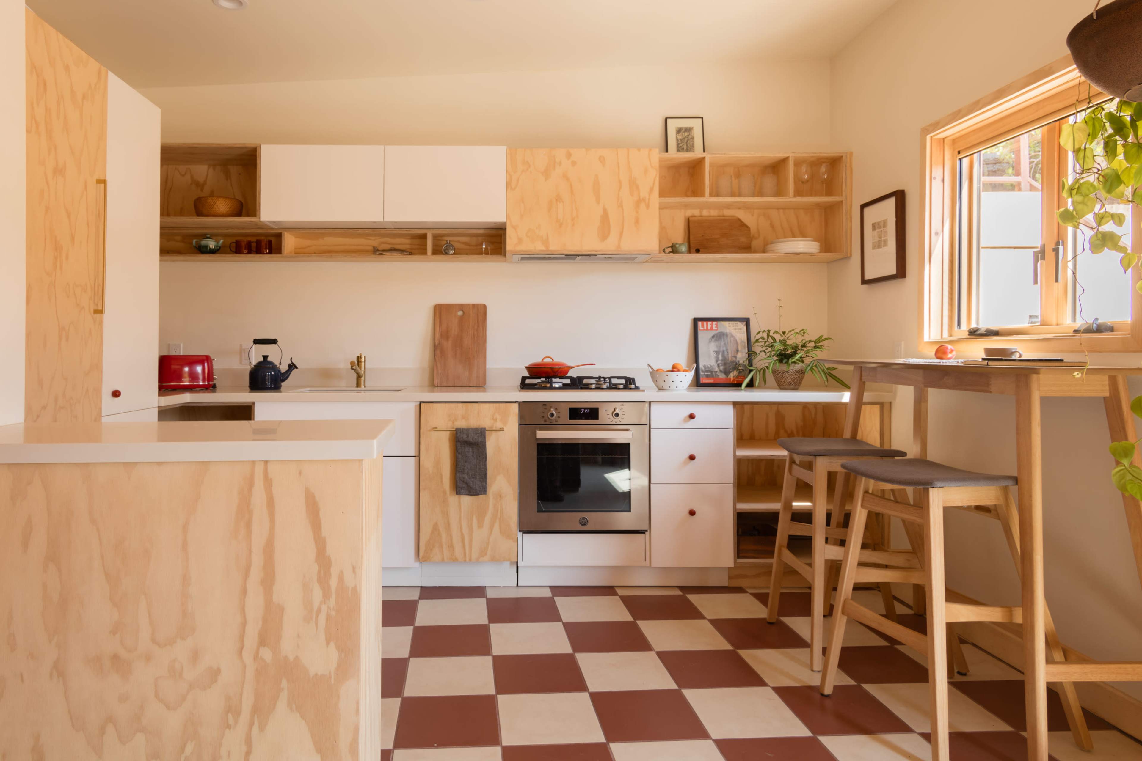 The kitchen features wooden cabinetry, a modern stove, and a dining area with tall stools beside a window.