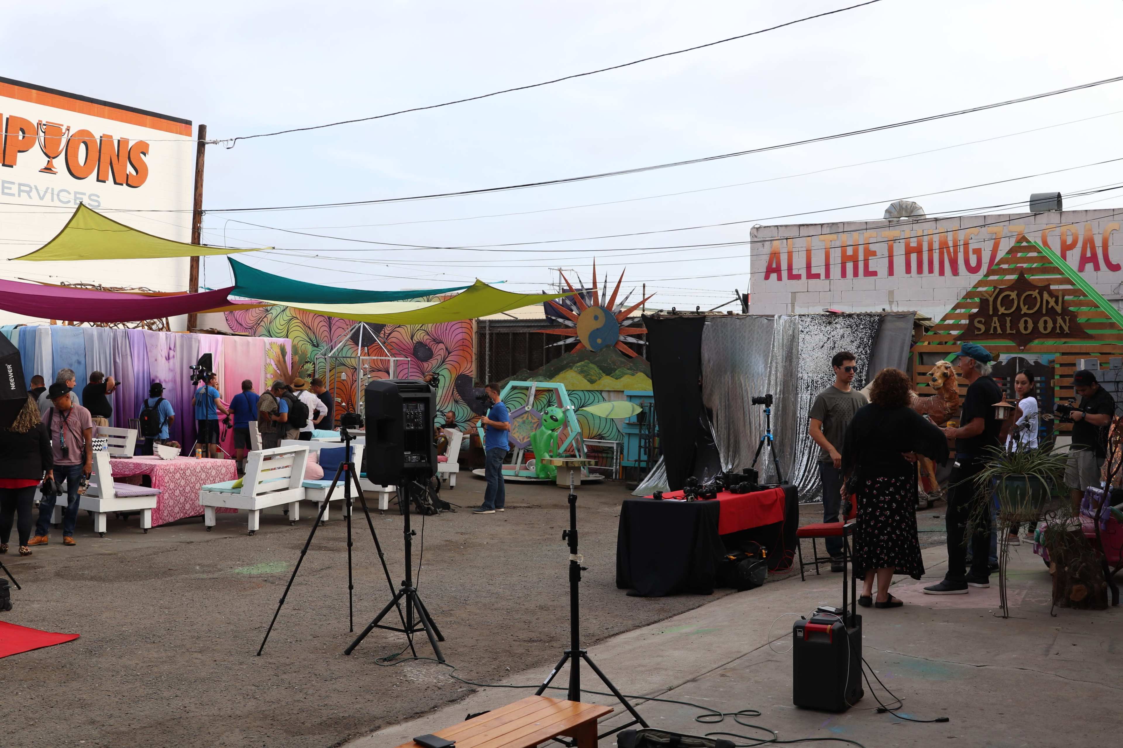 A vibrant outdoor setting with colorful decorations, seating arrangements, and a film crew preparing for a shoot.