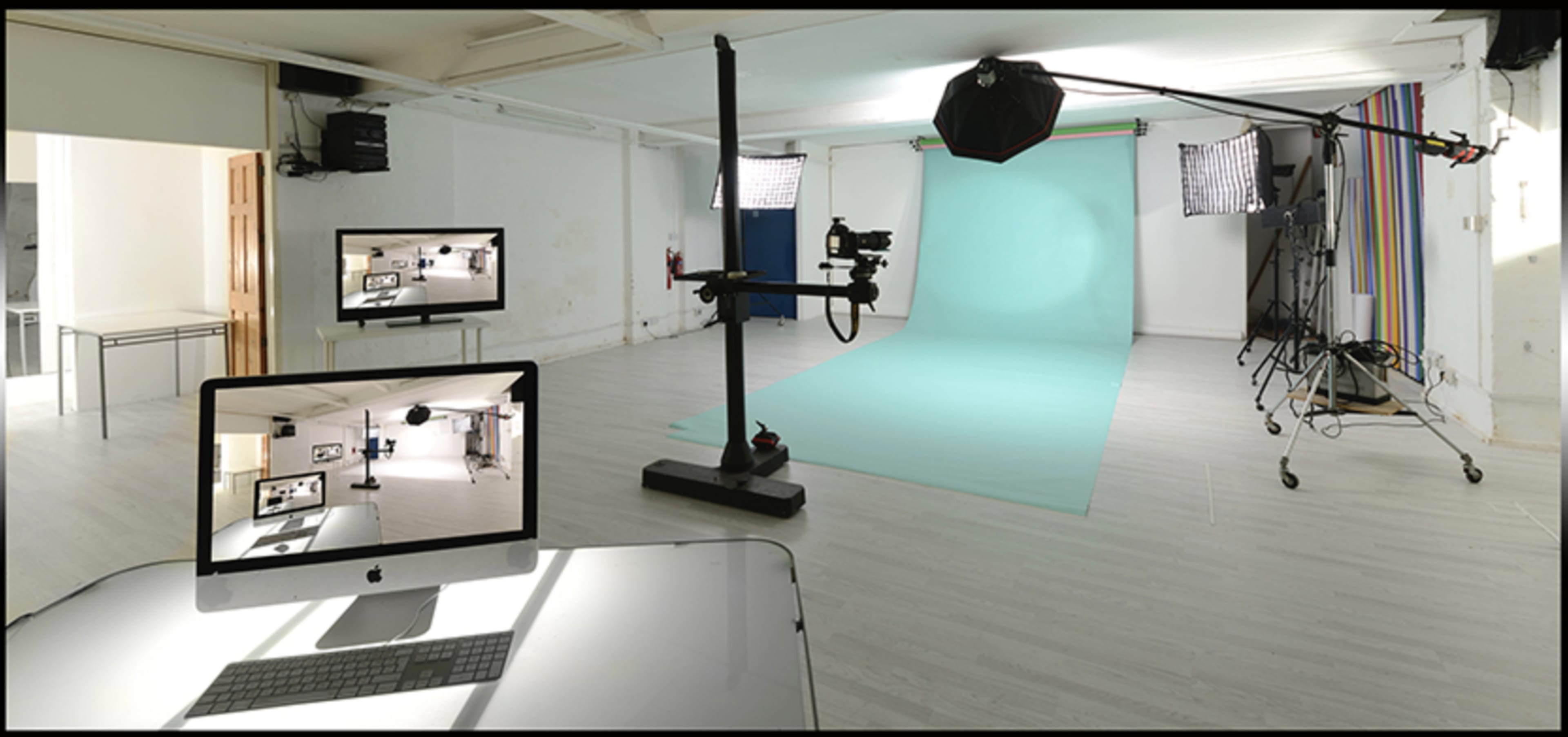 A photography studio equipped with a turquoise backdrop, lighting equipment, and a computer displaying a live video feed of the space.