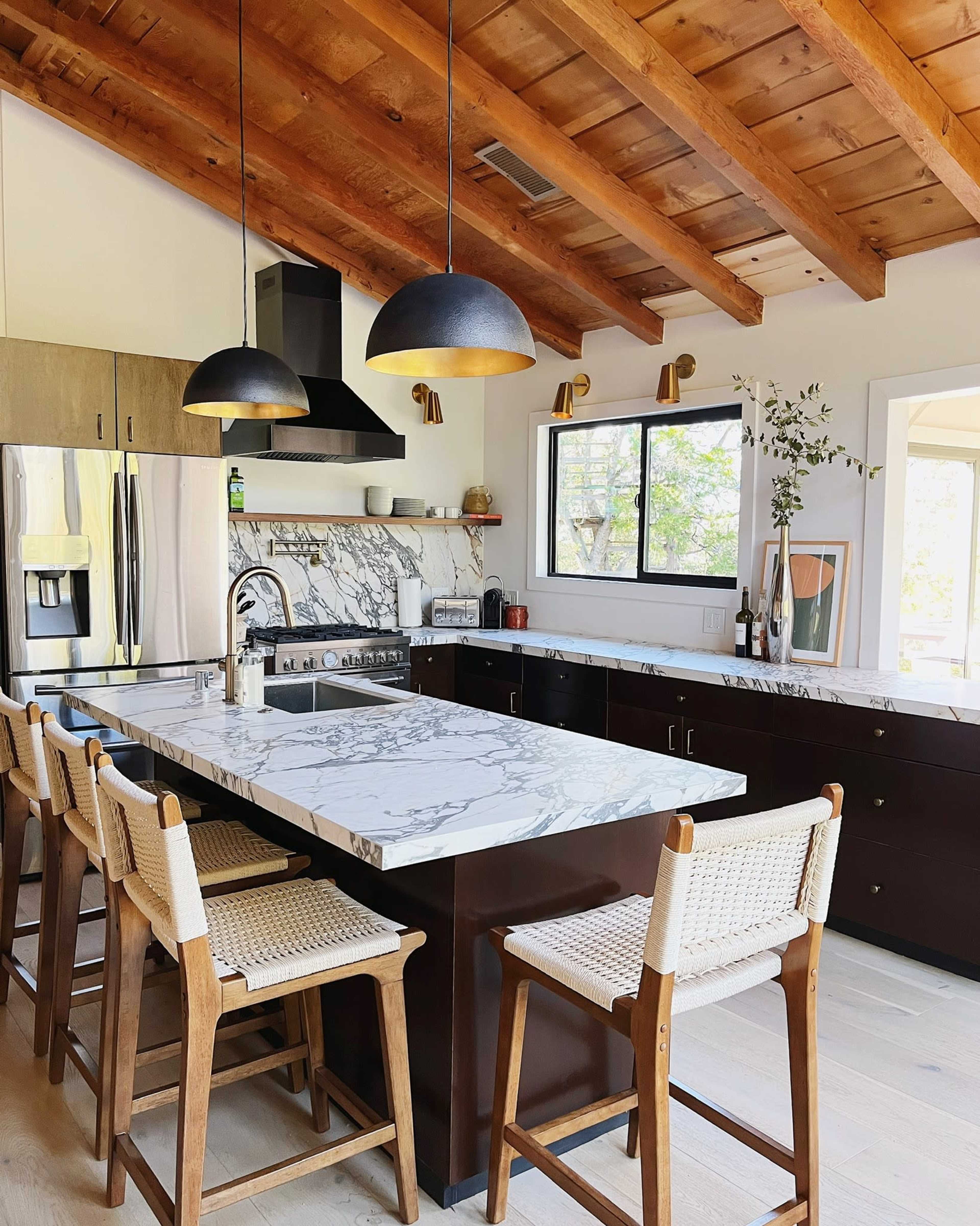 A contemporary kitchen with a marble island, wooden ceiling beams, and bar stools.