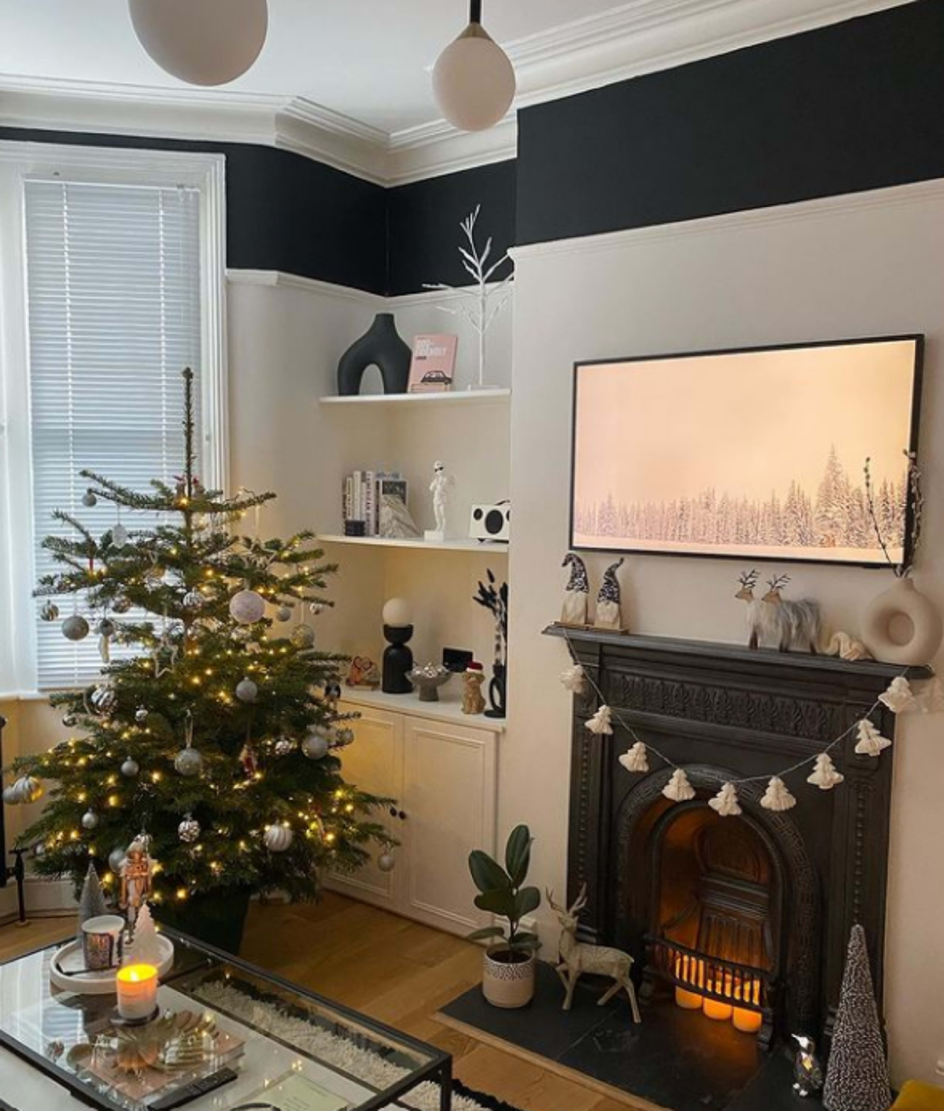 A living room decorated for the holidays, featuring a Christmas tree, a modern TV displaying a winter scene, and a fireplace with decorative elements.