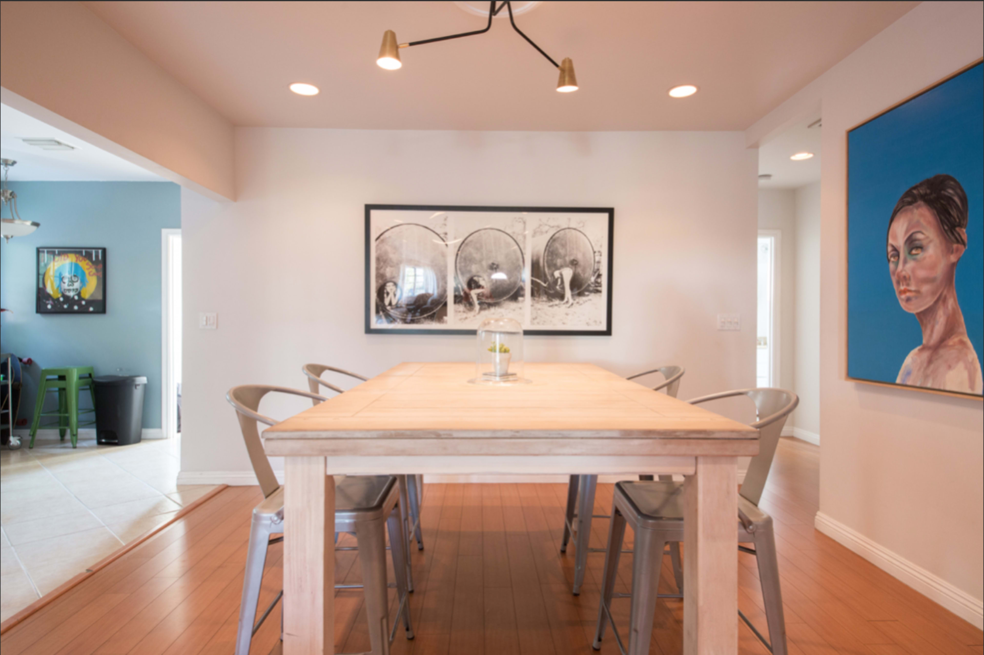 A spacious dining area features a wooden table surrounded by metal chairs, with artwork displayed on the walls.