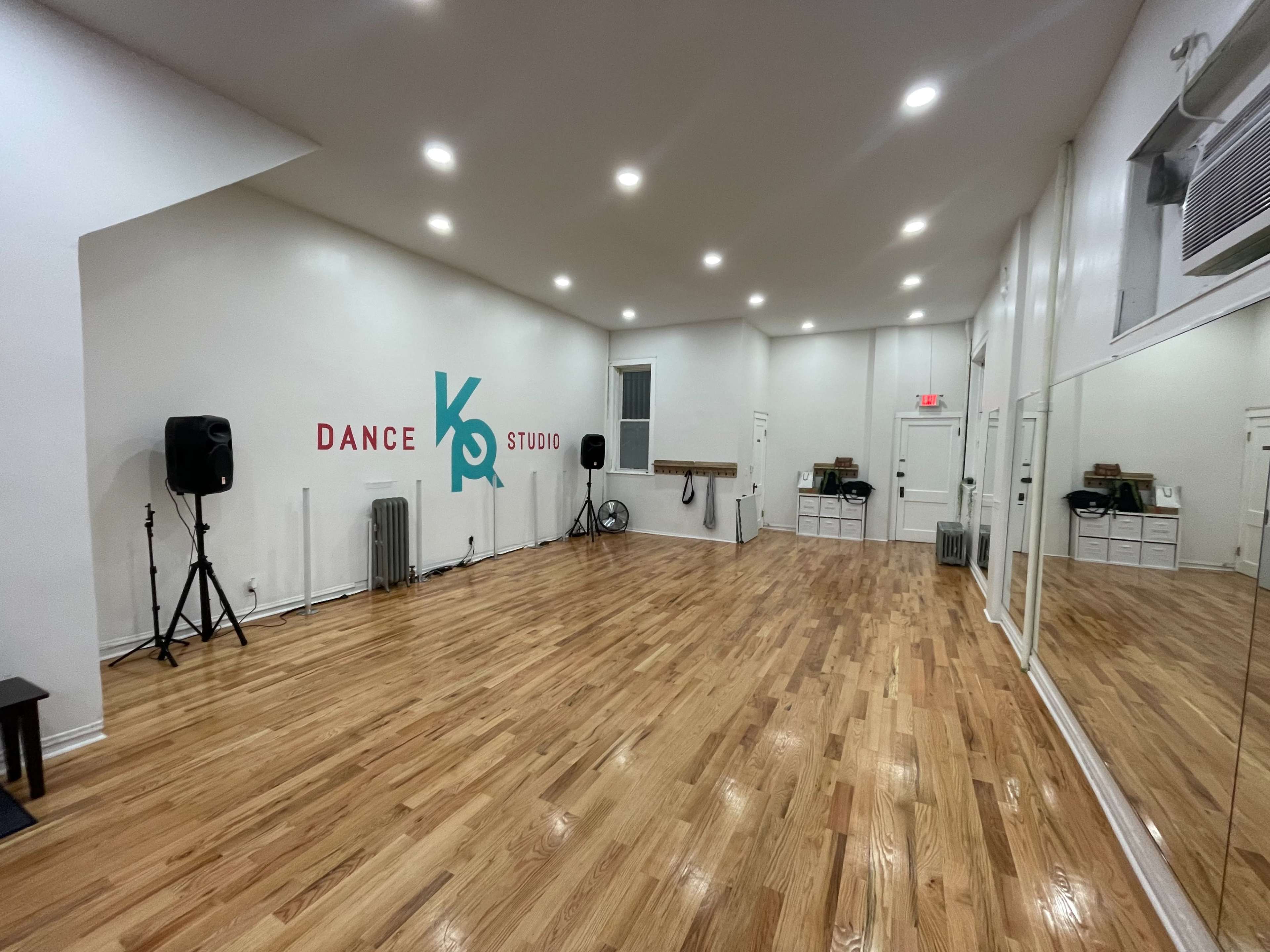 A spacious dance studio with wooden flooring, mirrors lining one wall, and the words "Dance Studio" in colorful lettering on the opposite wall.