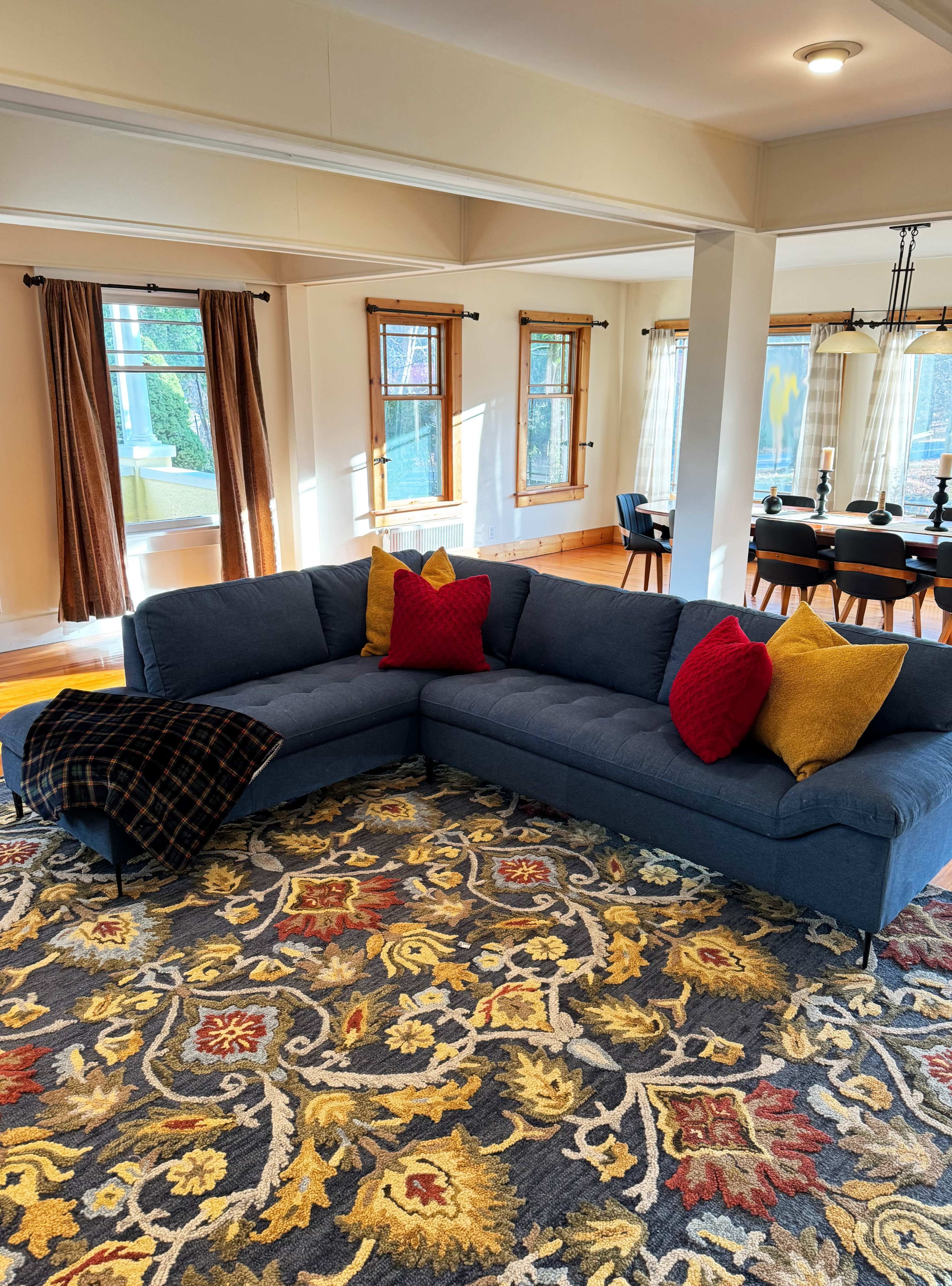 A blue sectional sofa with red and yellow pillows is positioned on a patterned area rug in a well-lit living room.