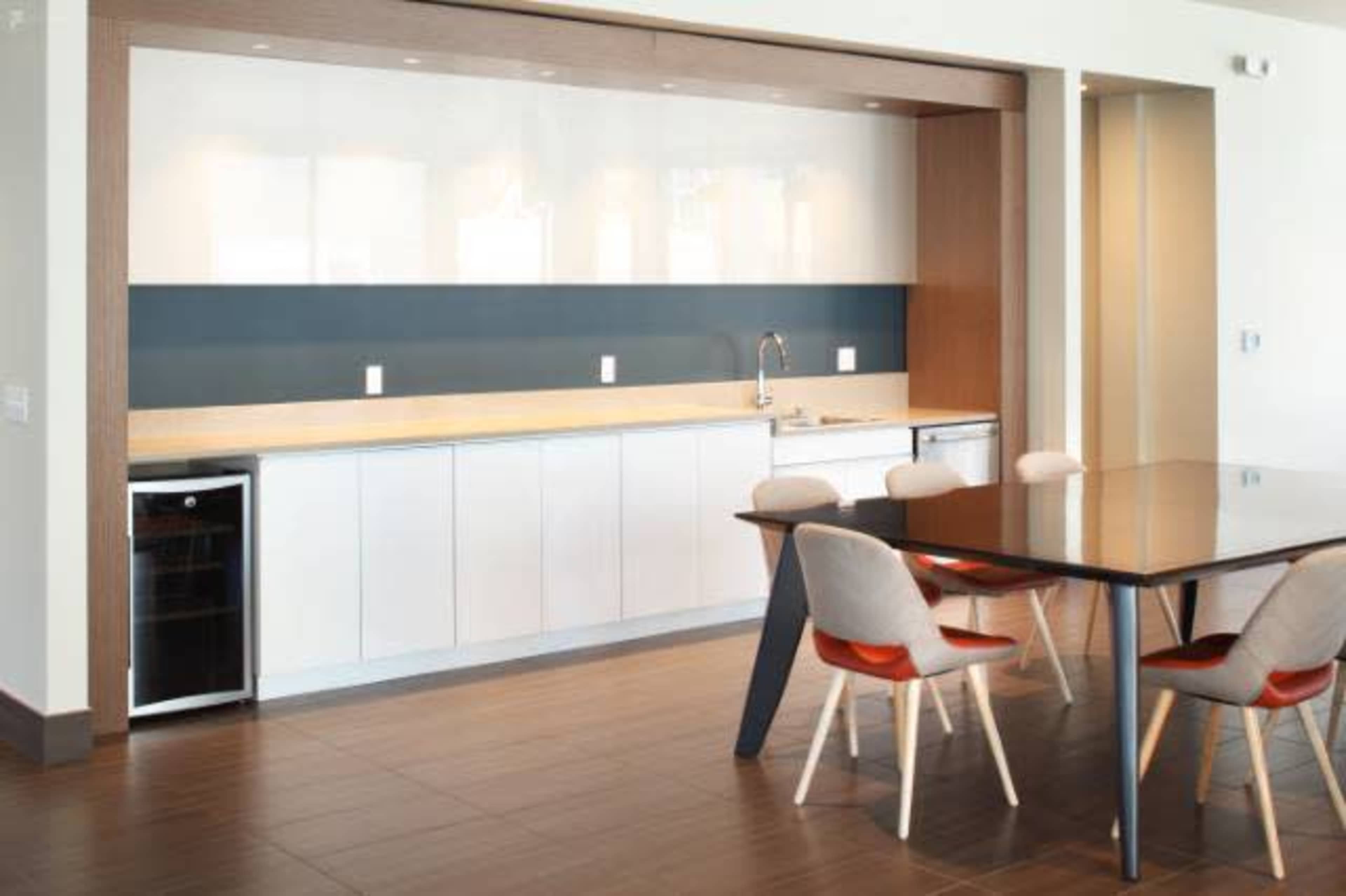 A modern kitchen features a sleek countertop with a sink, cabinets, and a dining table with chairs beside it.