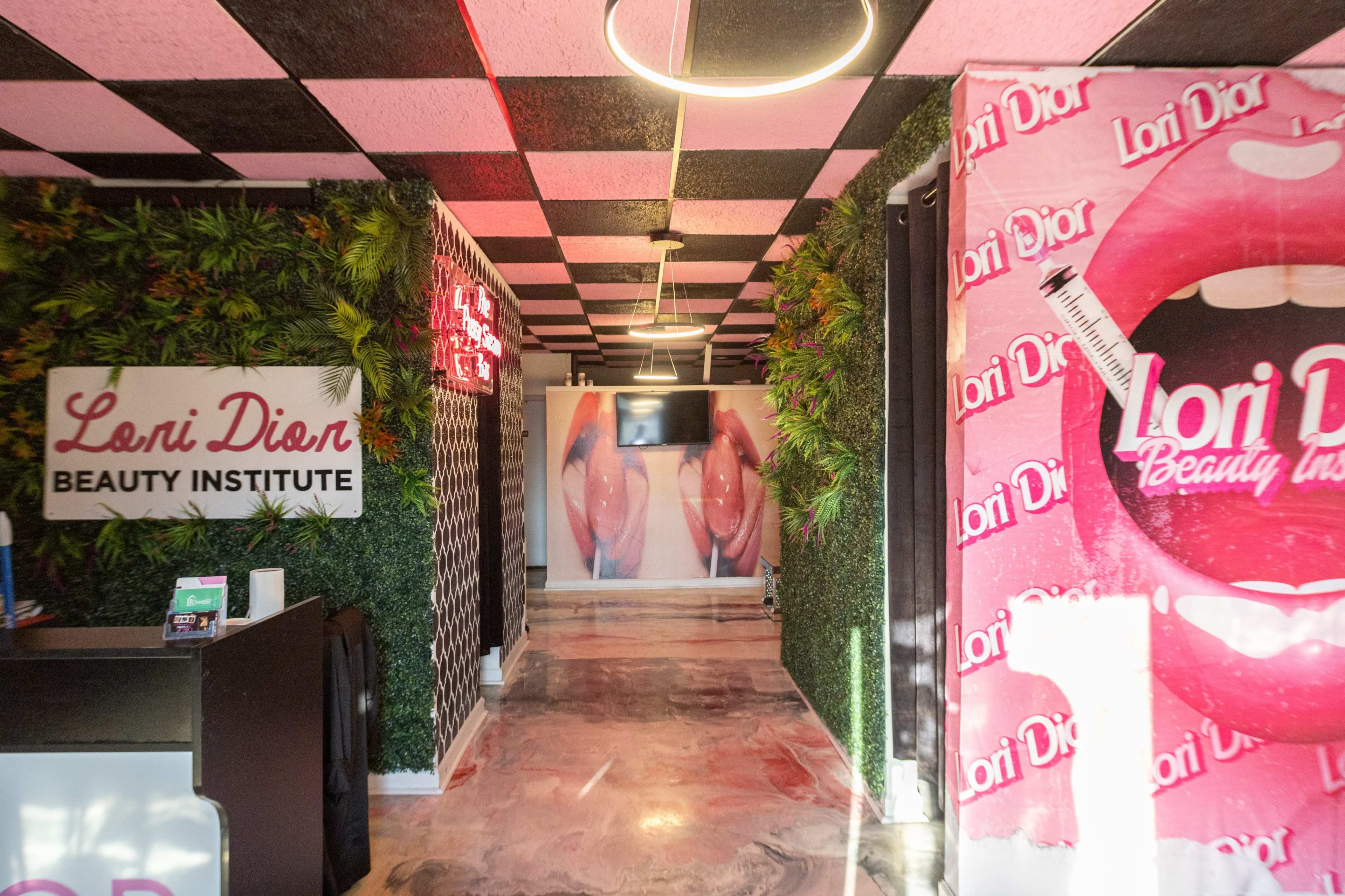 A hallway in the Loni Dion Beauty Institute featuring wall designs with pink and black colors and greenery along the sides.