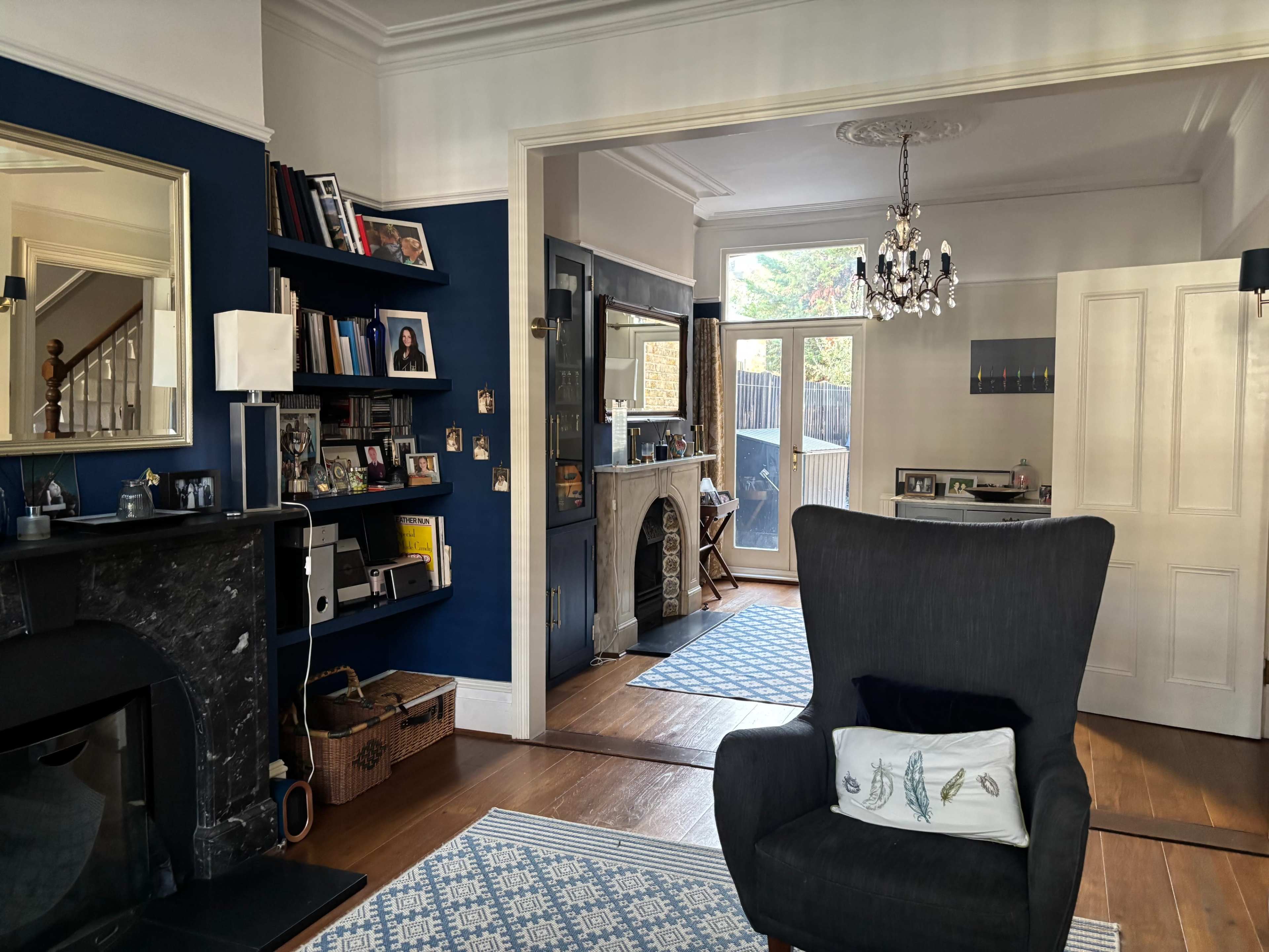 The image shows a living room with dark blue walls, a fireplace, a bookshelf filled with pictures and books, and a view of an adjacent room through an open door.