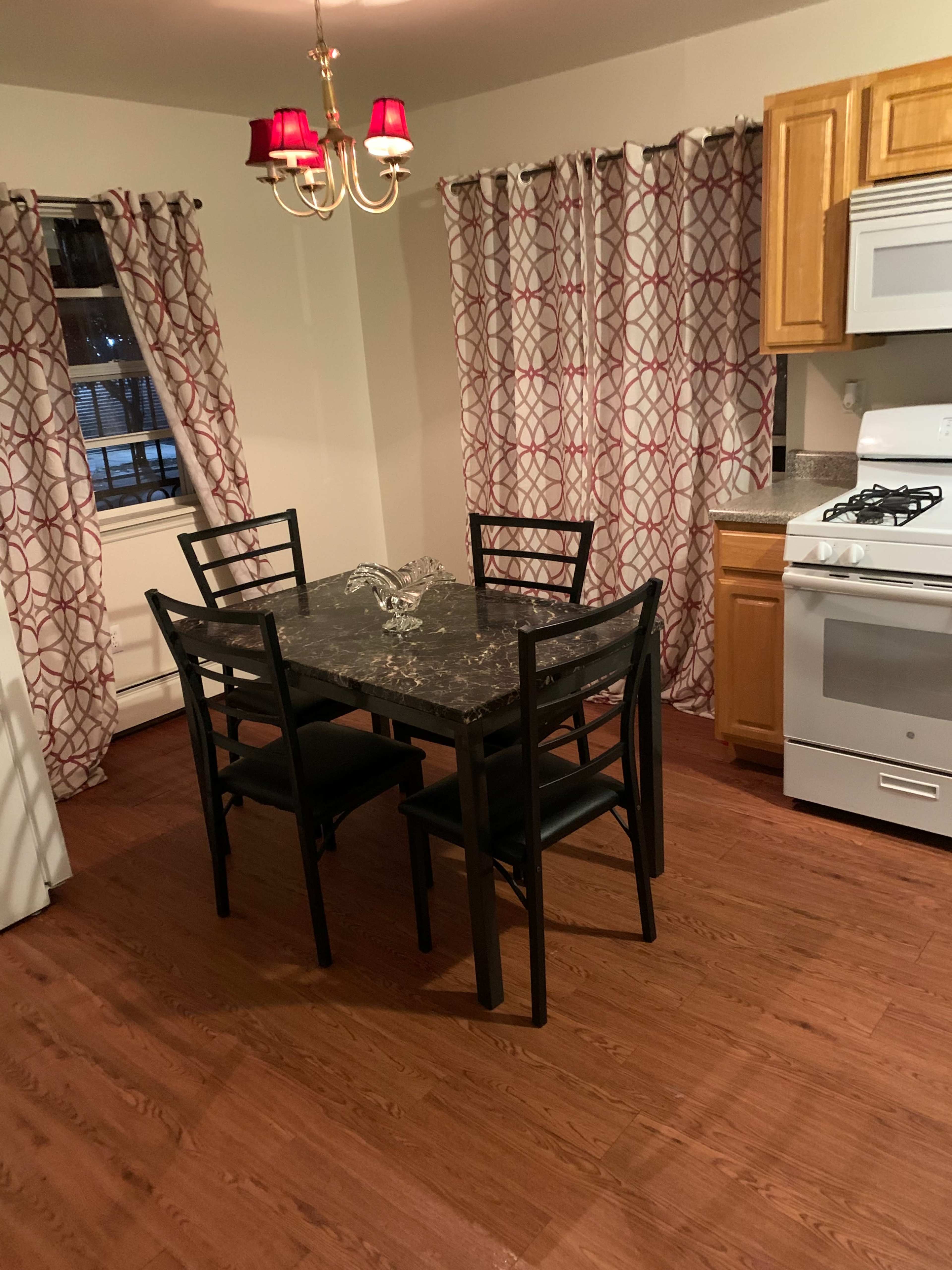 A kitchen features a round black table with four chairs, a stove, and cabinets, all accompanied by red and white patterned curtains.