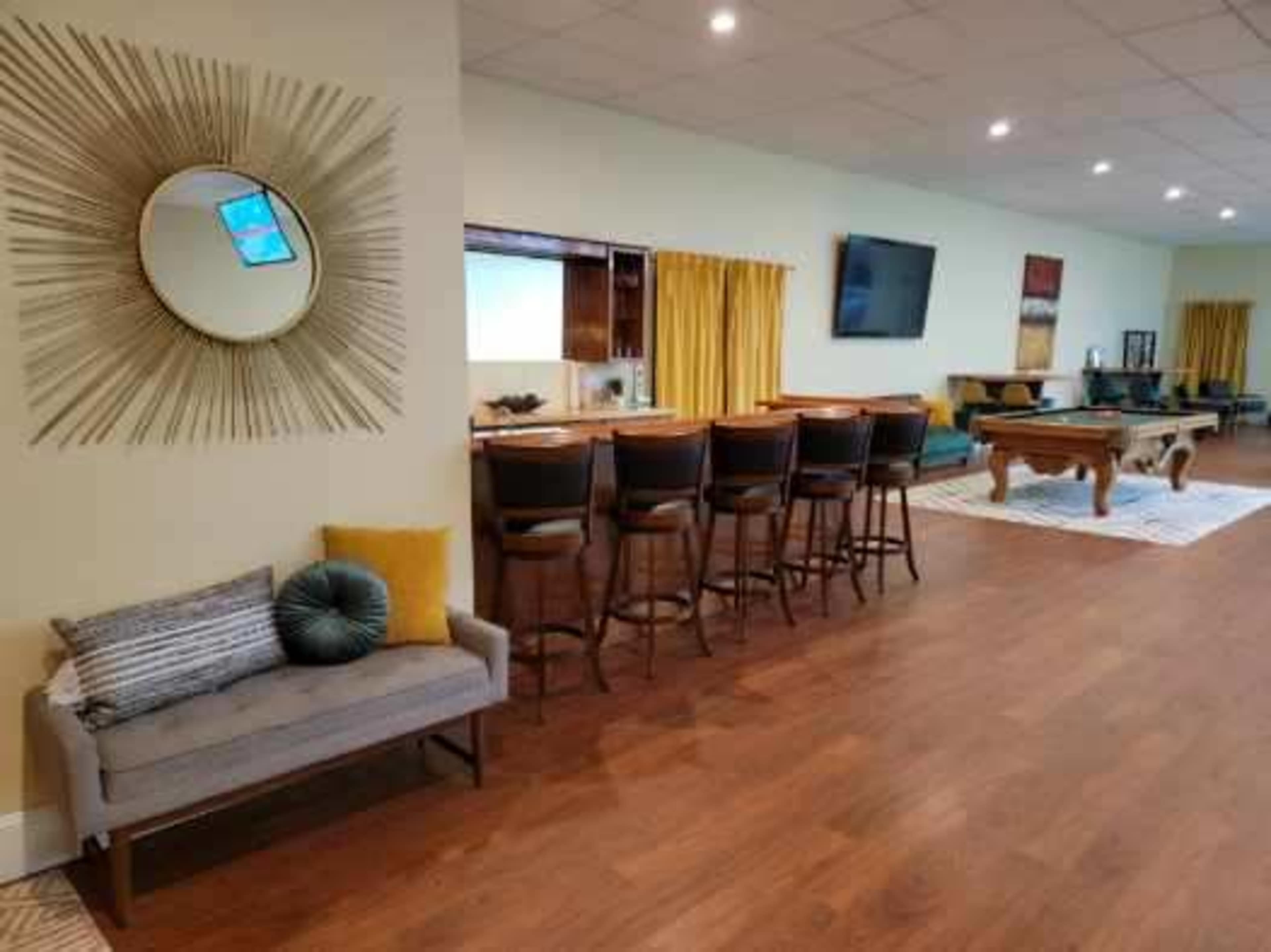 A large room featuring a bar with several high stools, a pool table, and a seating area with a couch and decorative cushions.
