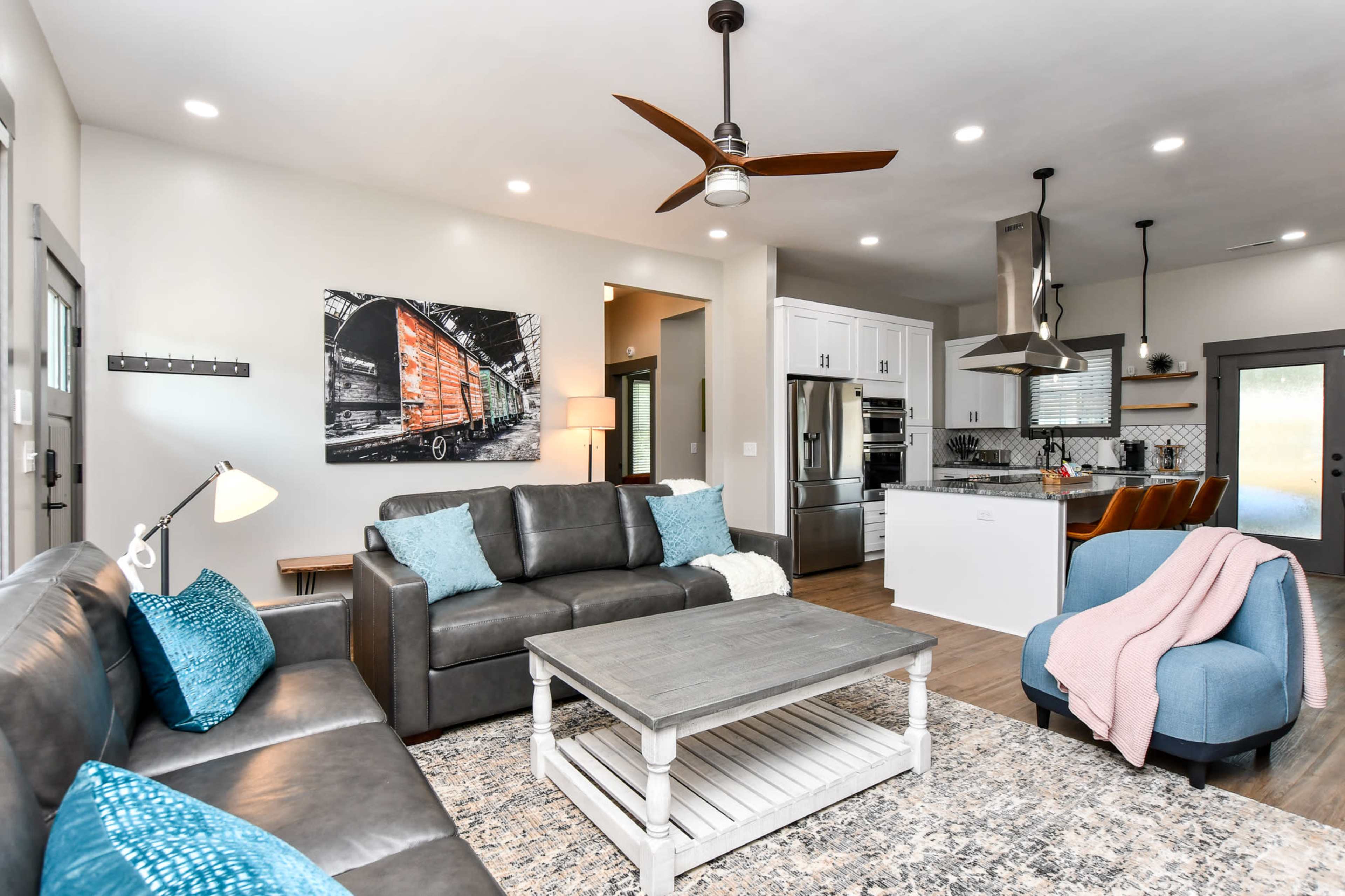 A modern living room featuring a gray sofa, a coffee table, and an adjoining kitchen area, all designed with a contemporary aesthetic.