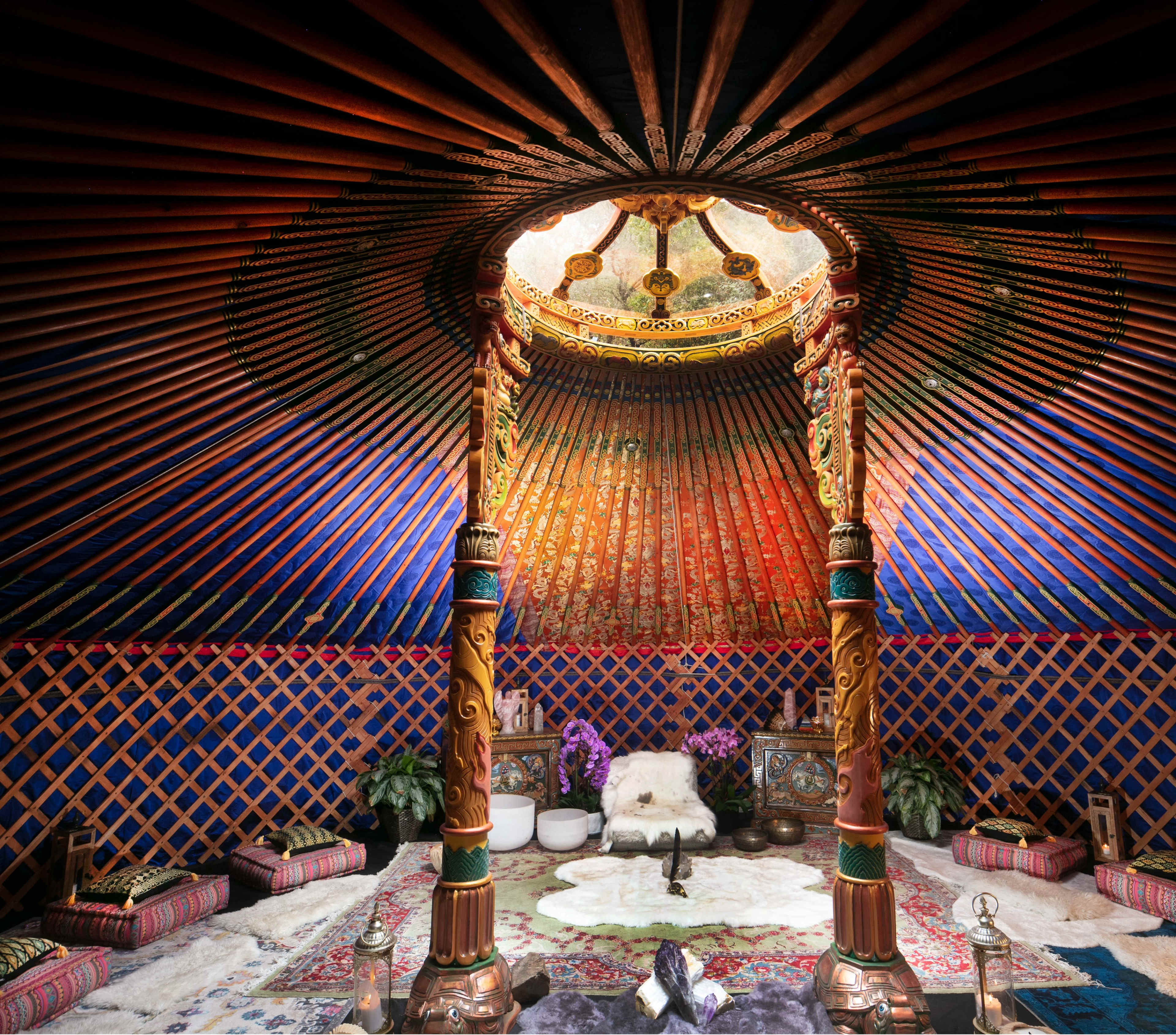 The image shows the interior of a traditional yurt decorated with colorful textiles, wooden pillars, and a circular skylight.