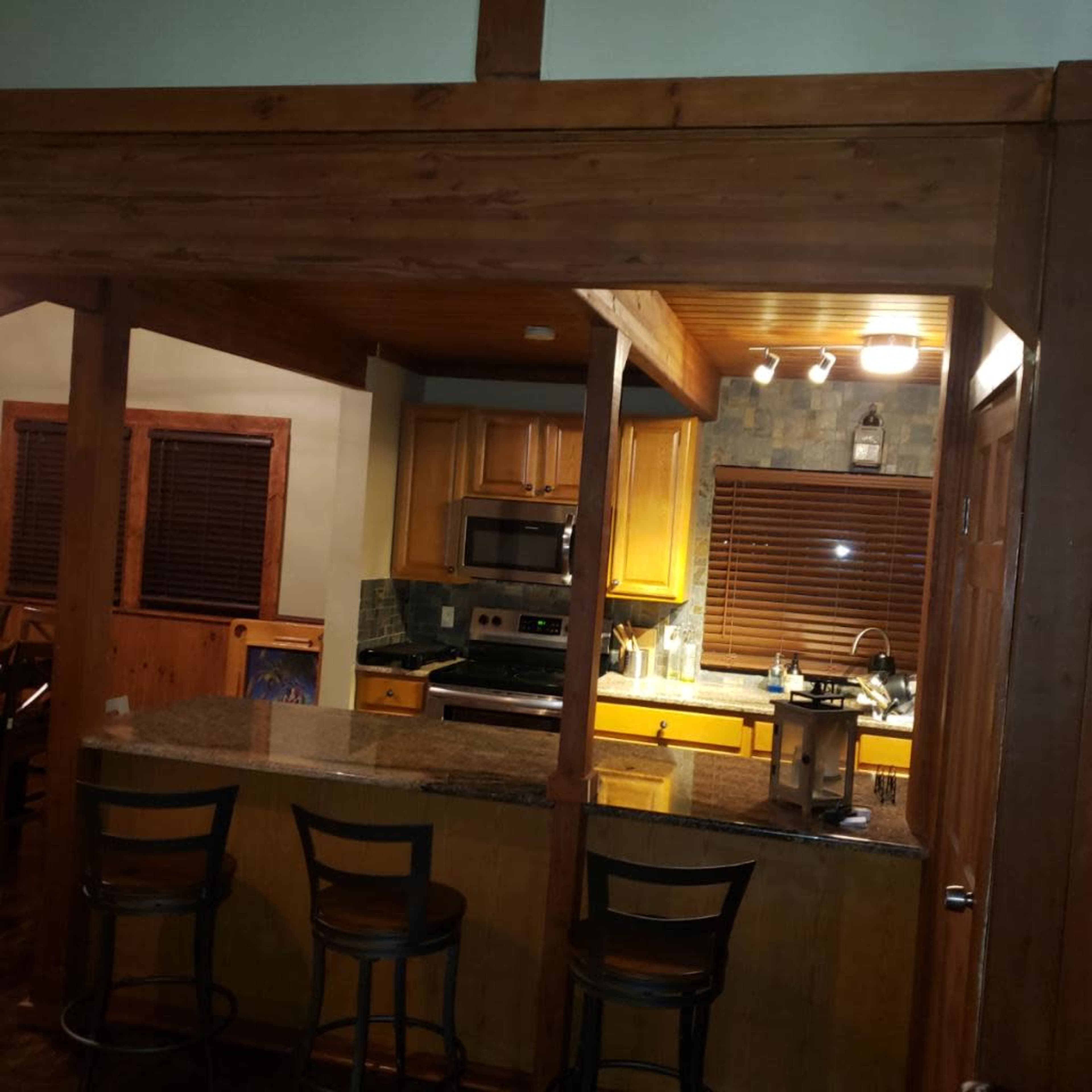 The image shows a kitchen area with wooden beams, granite countertops, and stainless steel appliances.