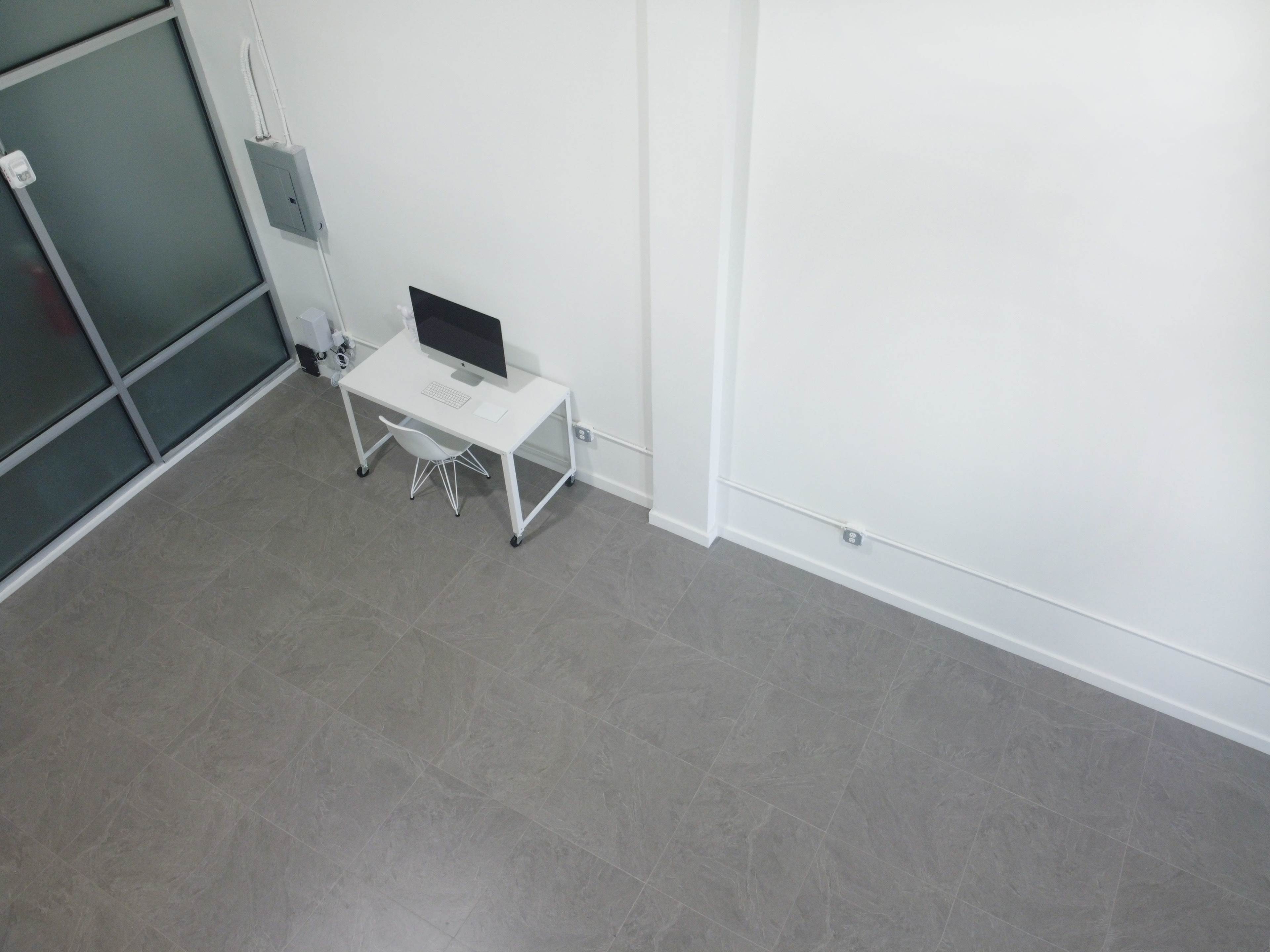 An aerial view of a minimalist workspace featuring a desk with a computer and a white chair on a stone tile floor.