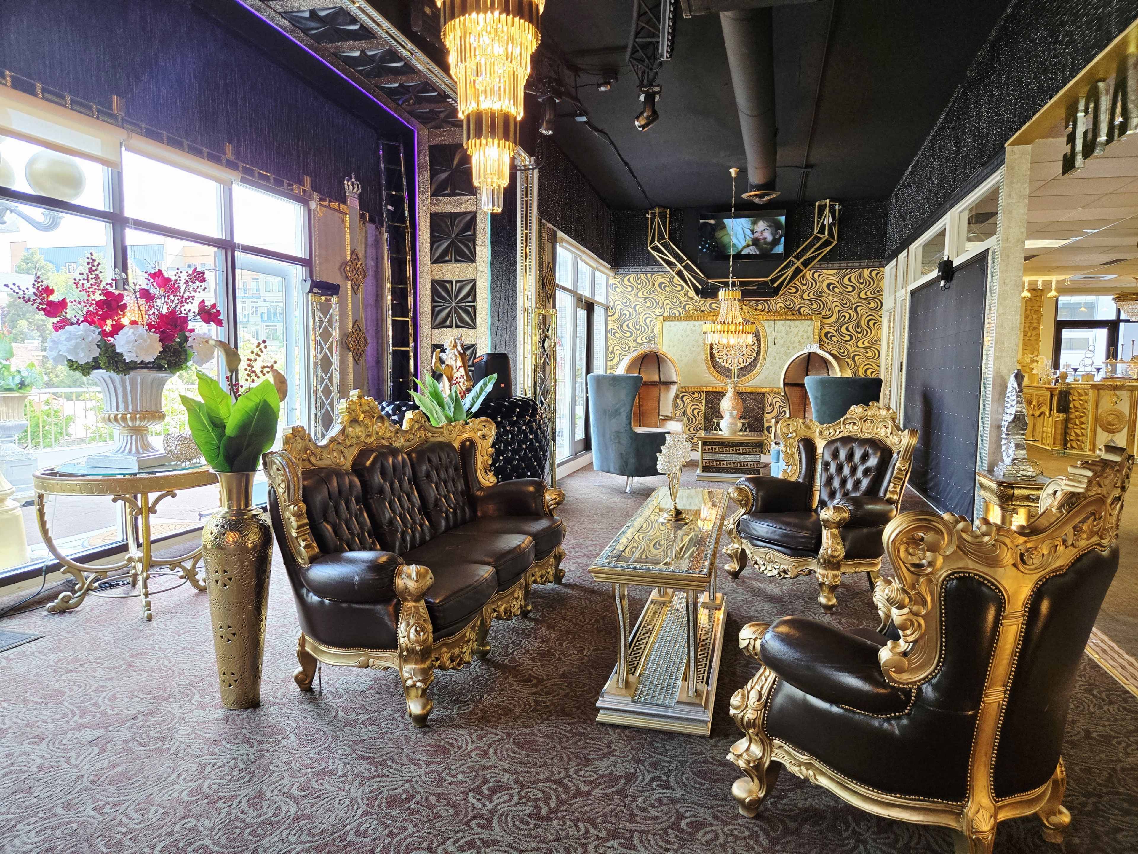 The image depicts an opulent interior featuring ornate golden furniture, plush seating, and large decorative plants, with bright natural light streaming through large windows.