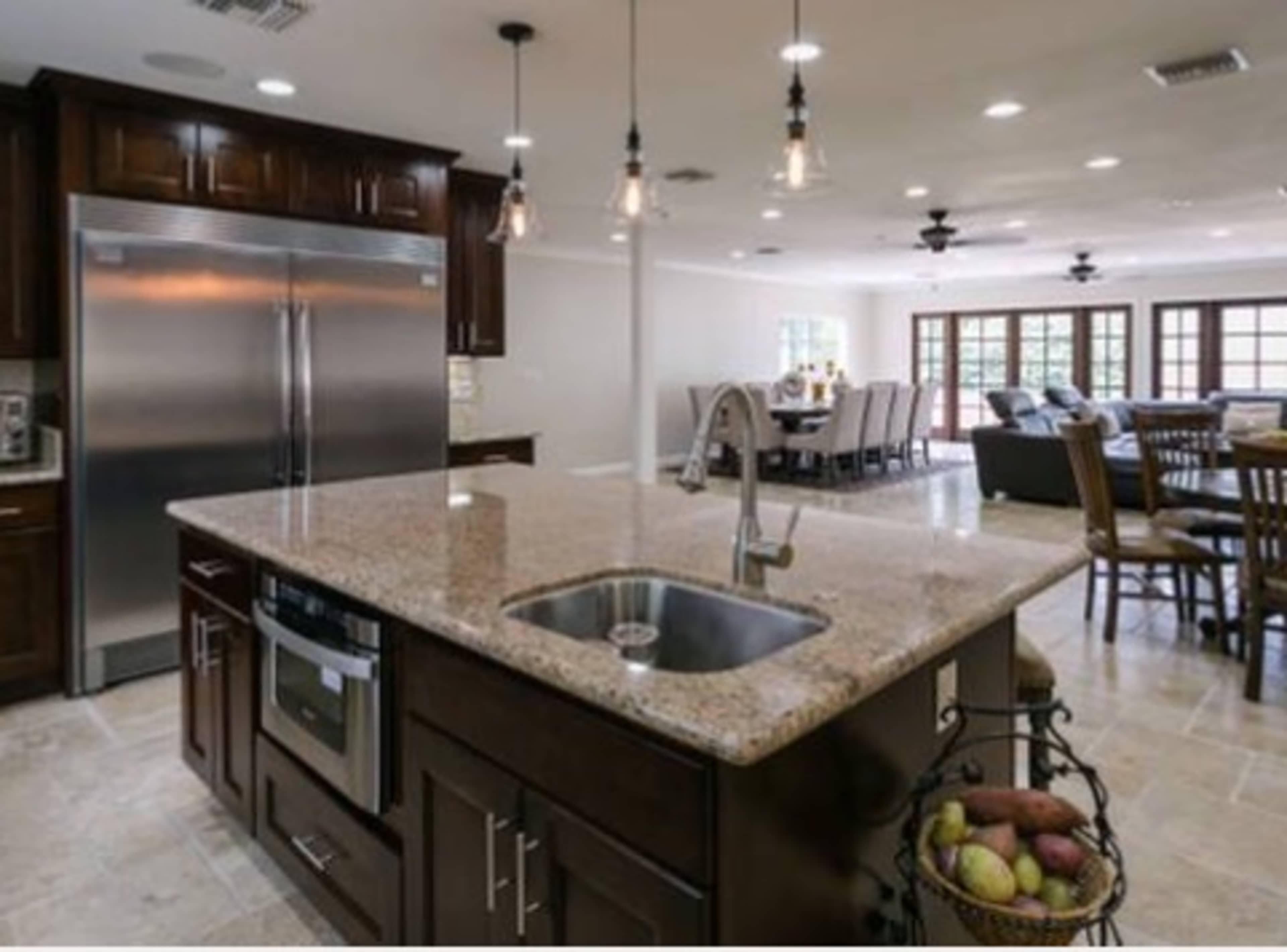 The image shows a modern kitchen featuring dark wood cabinets, a large granite island with a sink, and stainless steel appliances.
