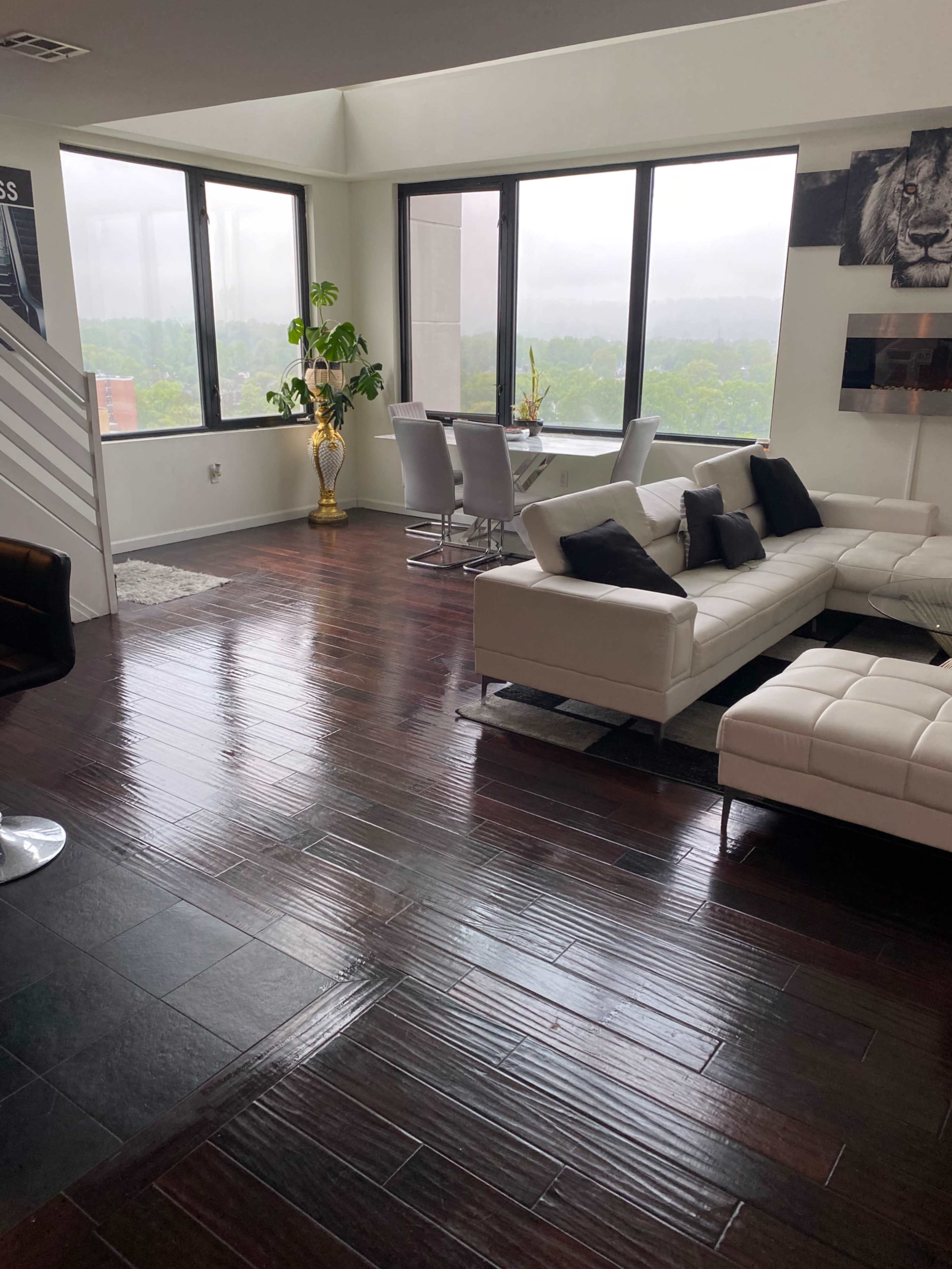 A modern living space with a white sectional sofa, a dining area with four chairs, large windows, and polished wooden floors.