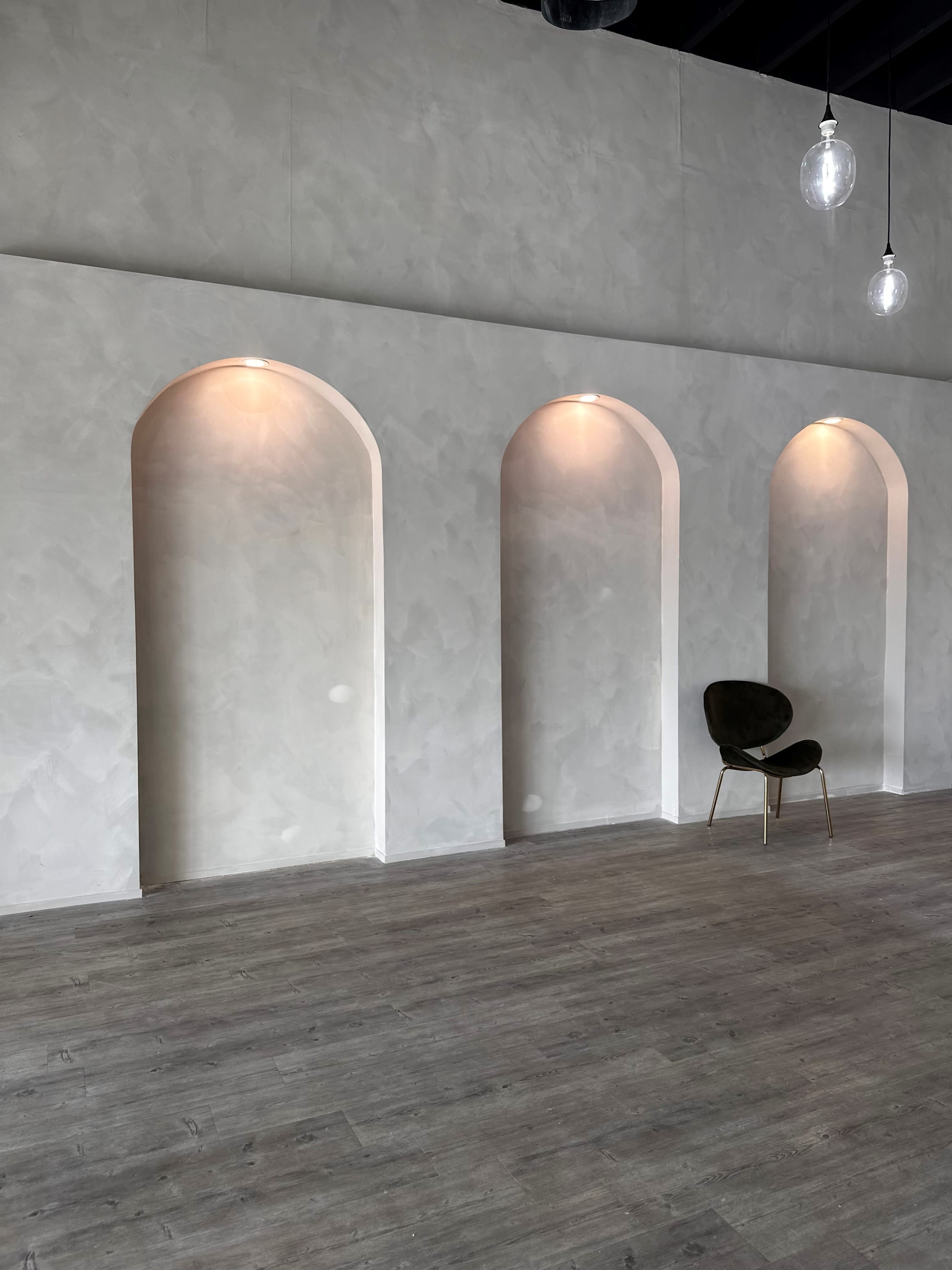 A minimalist interior space featuring three arched wall recesses and a single chair placed against a light-colored textured wall.