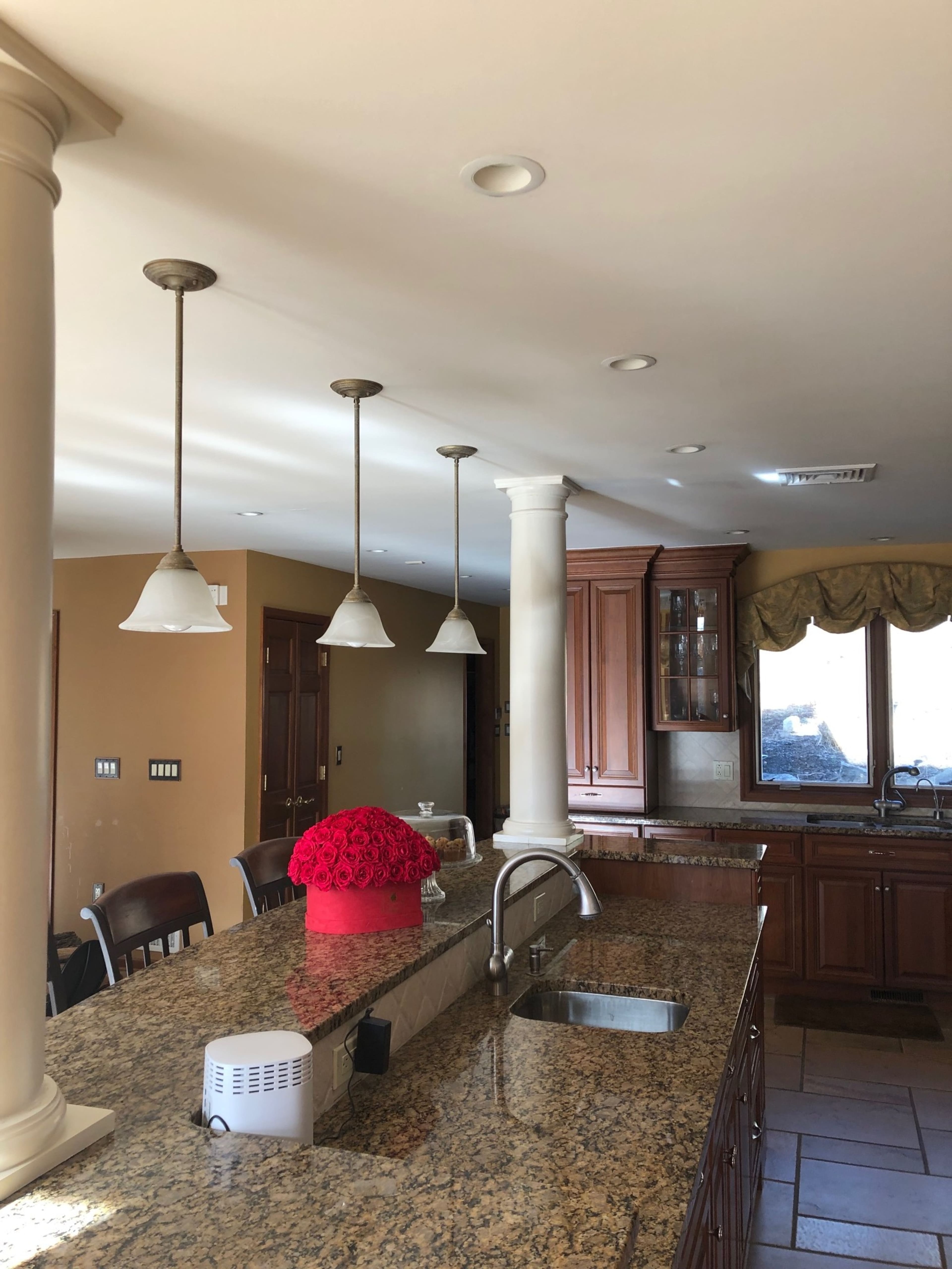 A kitchen with granite countertops, pendant lighting, and wooden cabinetry, featuring a vase of red flowers on the island.