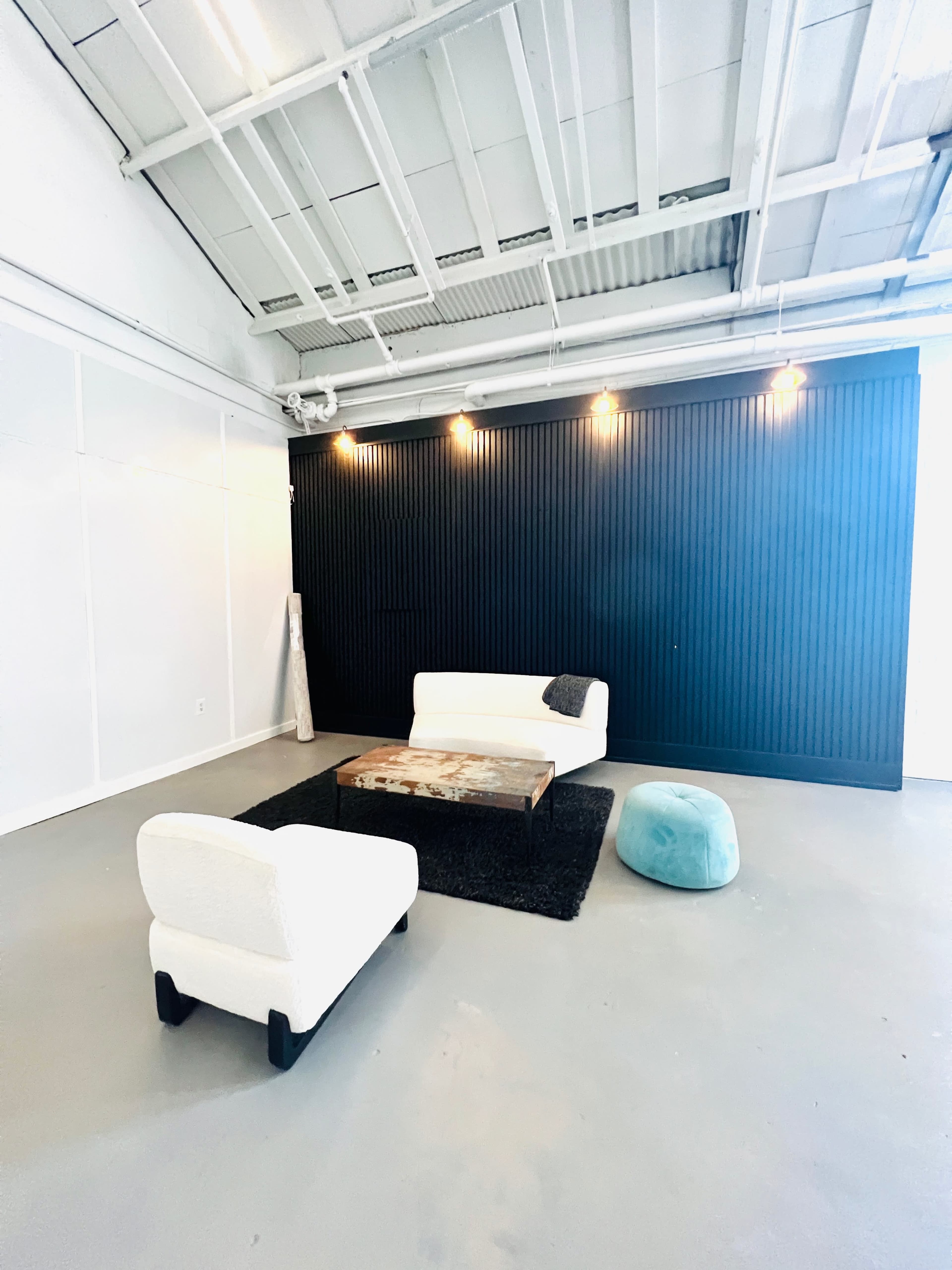 A modern living room with a white sofa and armchair around a wooden coffee table, set against a contrasting black wall with overhead lighting.