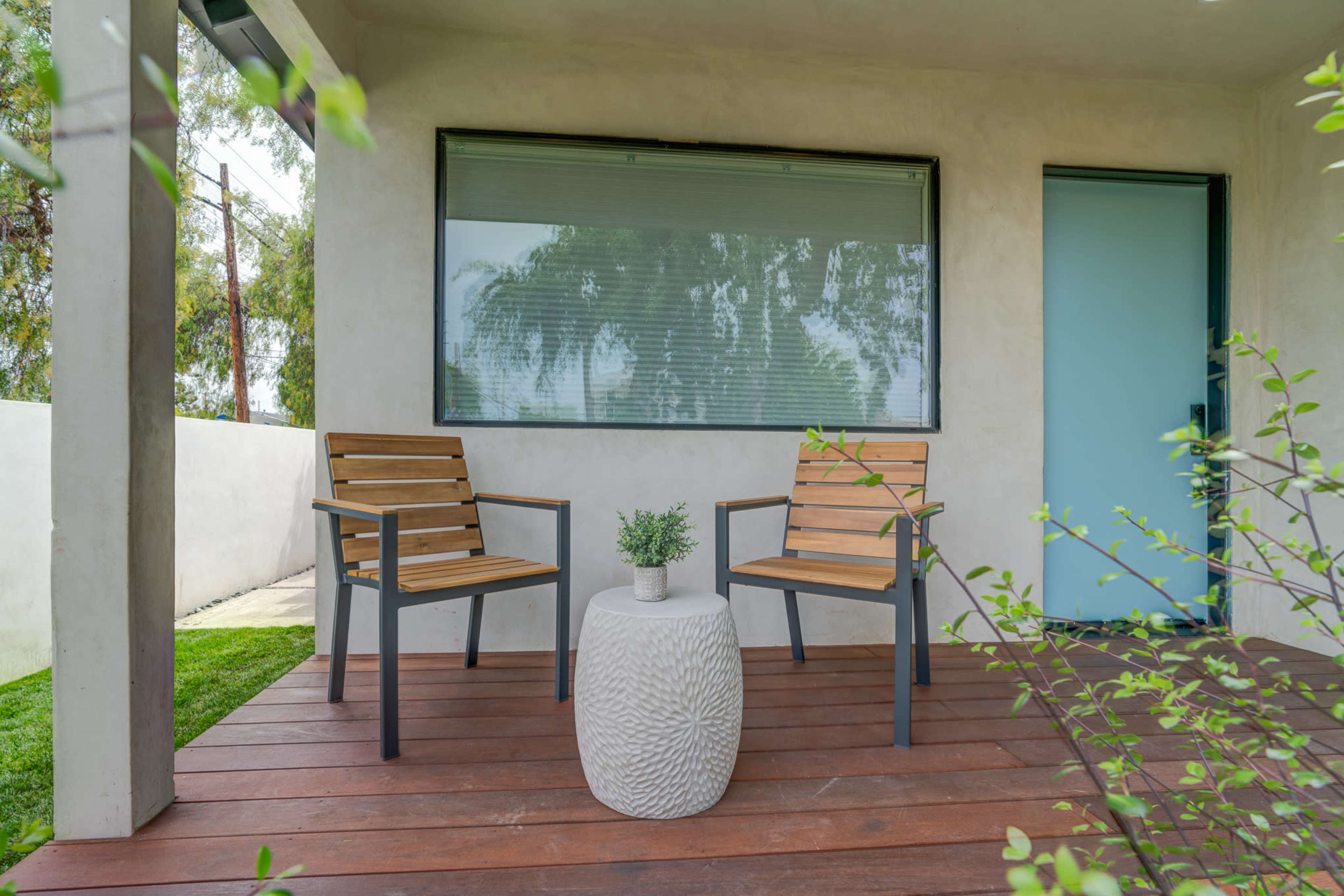 A small outdoor seating area features two wooden chairs and a textured round table with a potted plant on a deck.