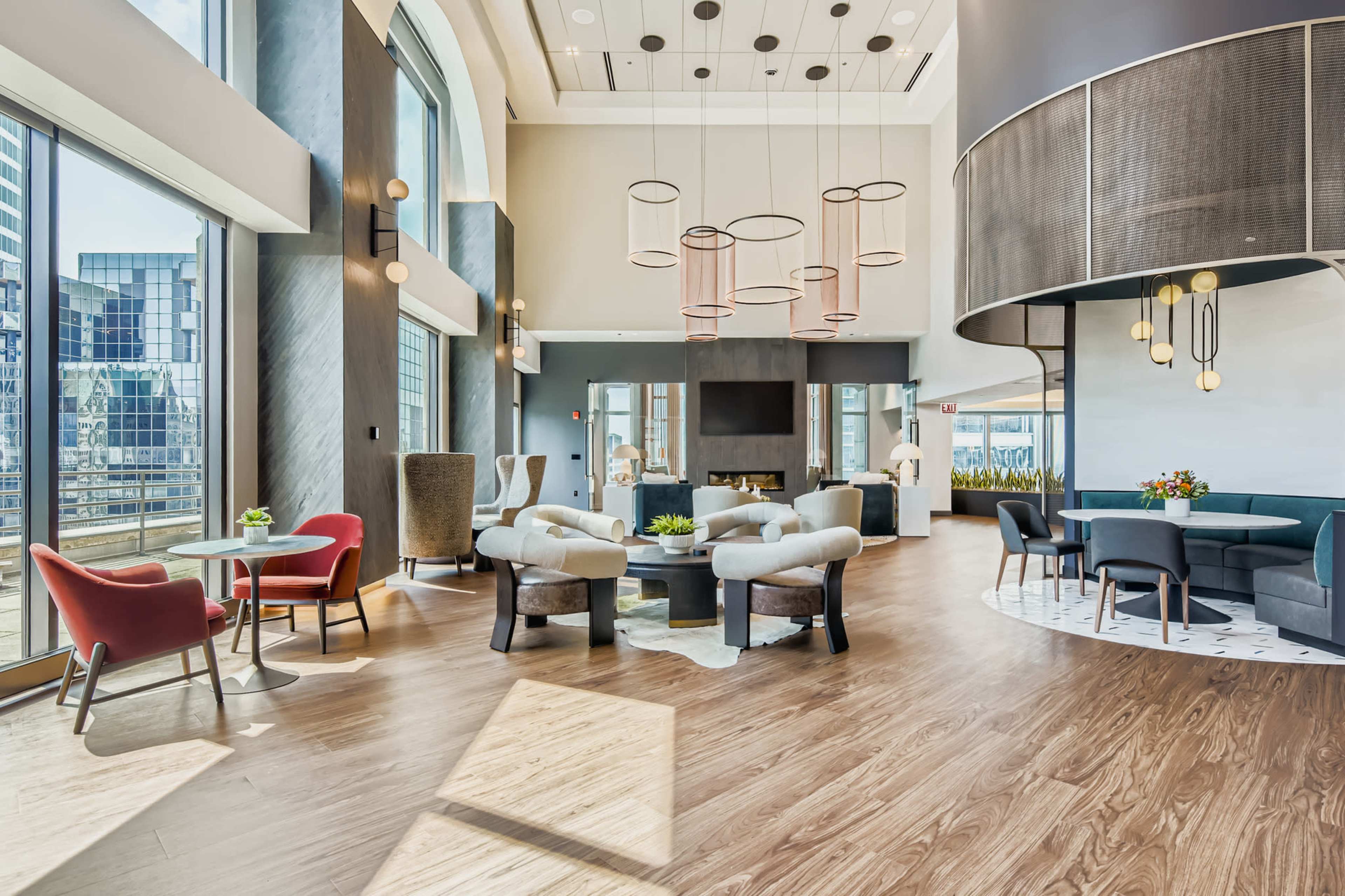 The image shows a modern lounge area with large windows, various seating options, and decorative lighting fixtures.