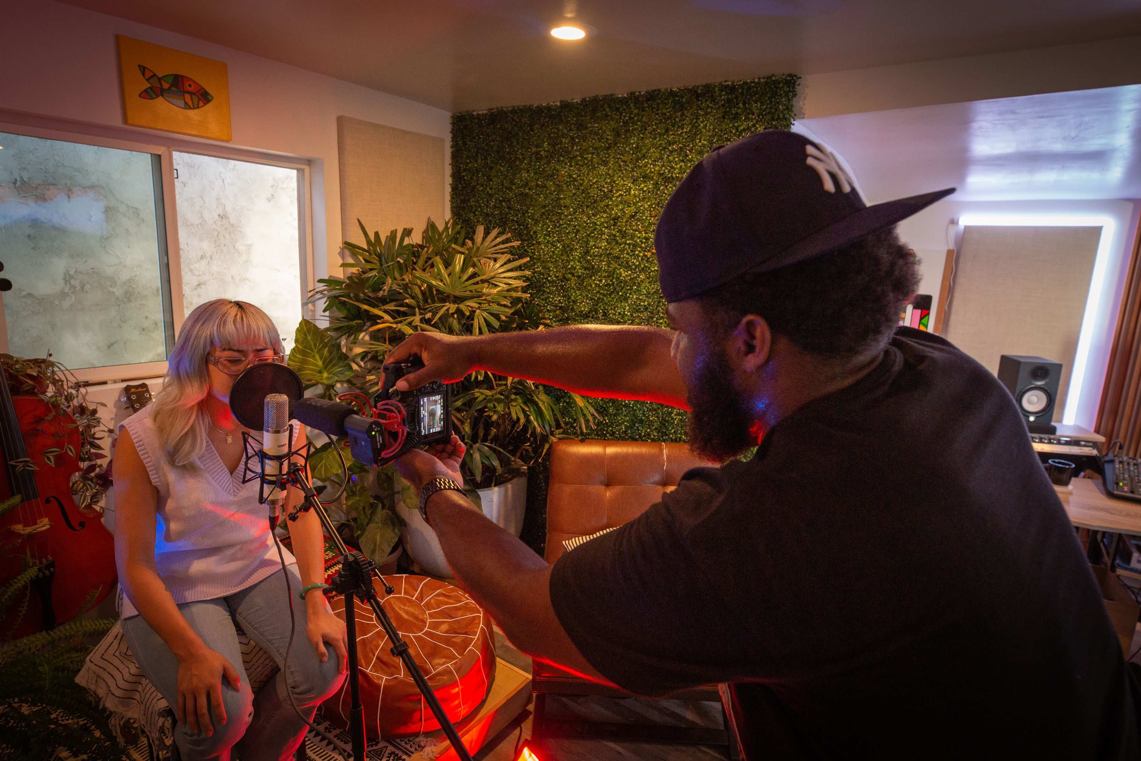 A person records a woman speaking into a microphone in a cozy, well-decorated studio.