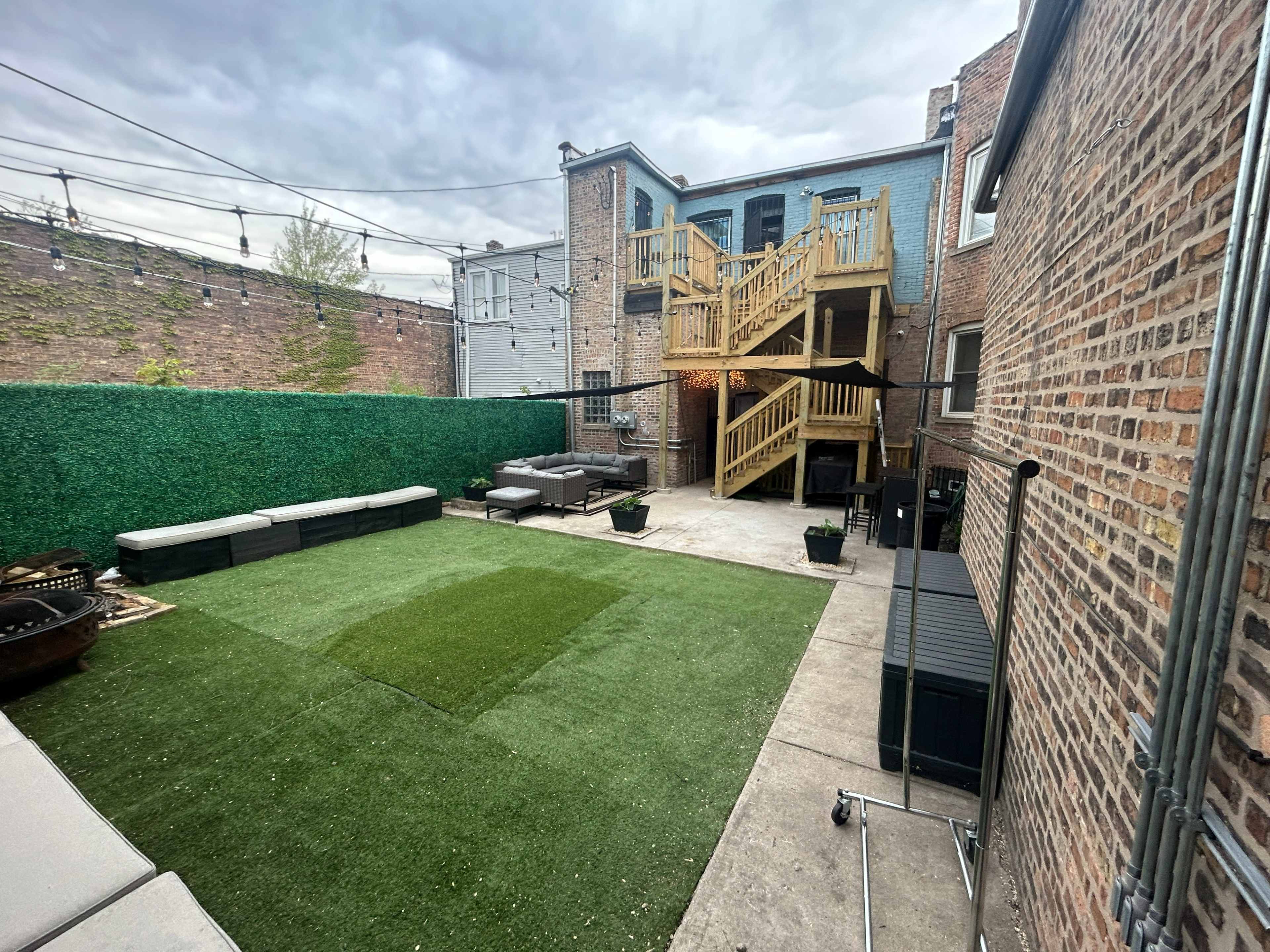 A backyard area with artificial turf, a wooden staircase leading to a building, and several seating arrangements along the edges.
