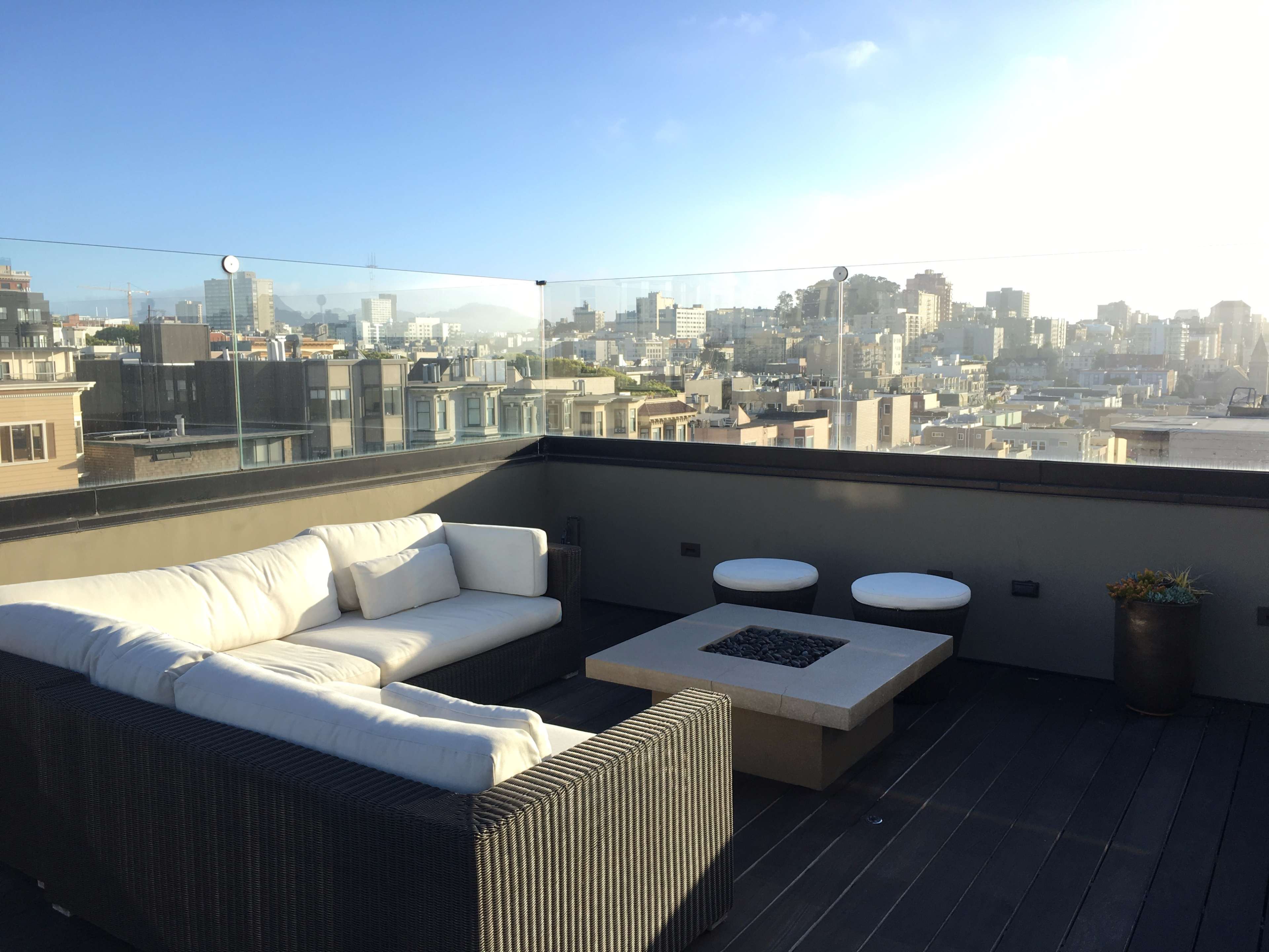 A rooftop terrace features a modern sectional sofa, a fire pit, and city skyline views.