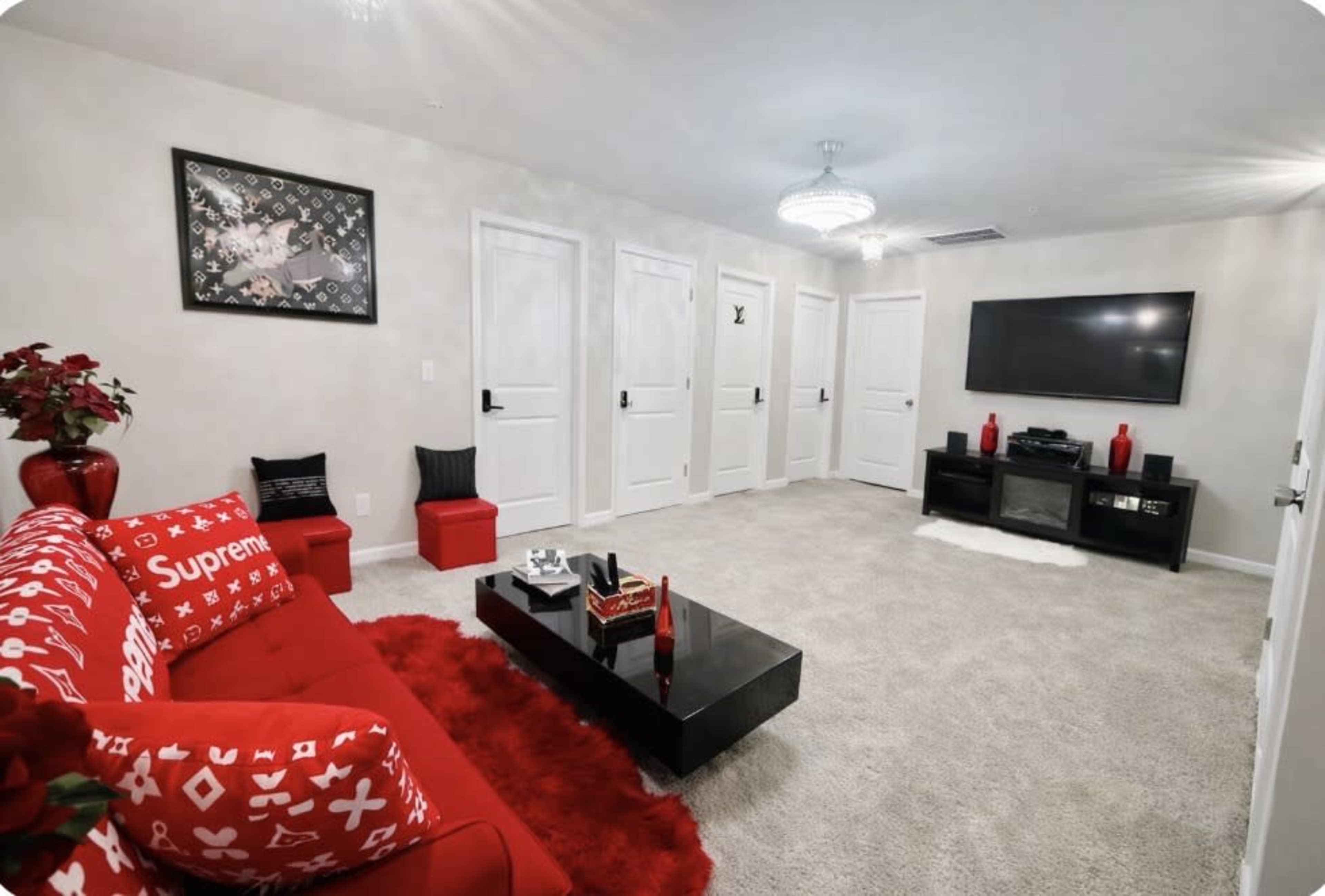 The living room features a red couch, a black coffee table, and a wall-mounted television with multiple white doors in the background.