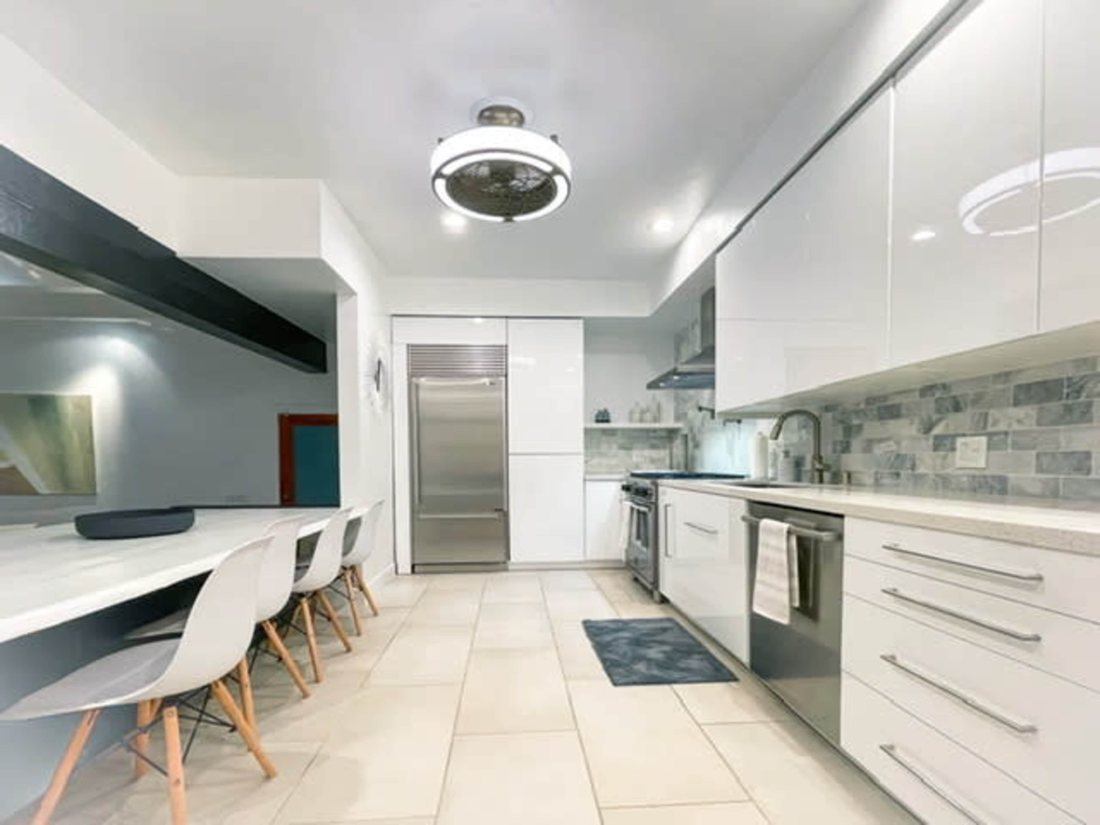 A modern kitchen featuring sleek white cabinets, stainless steel appliances, and a long dining table with white chairs.
