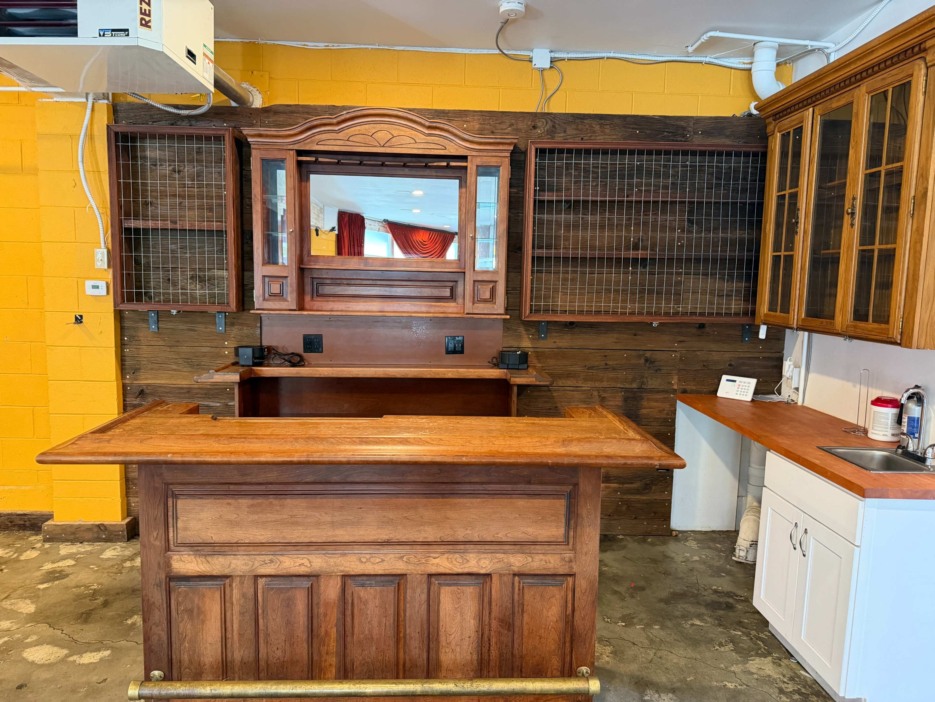 The image shows a wooden countertop with a mirror-backed wooden structure and cabinets against a bright yellow wall.